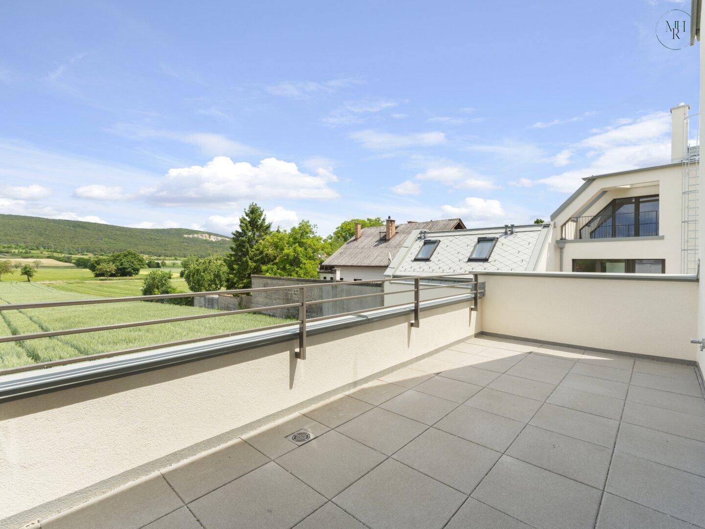 Große Dachterrasse mit Fliesenboden und weitem Blick über grüne Felder und Hügel.