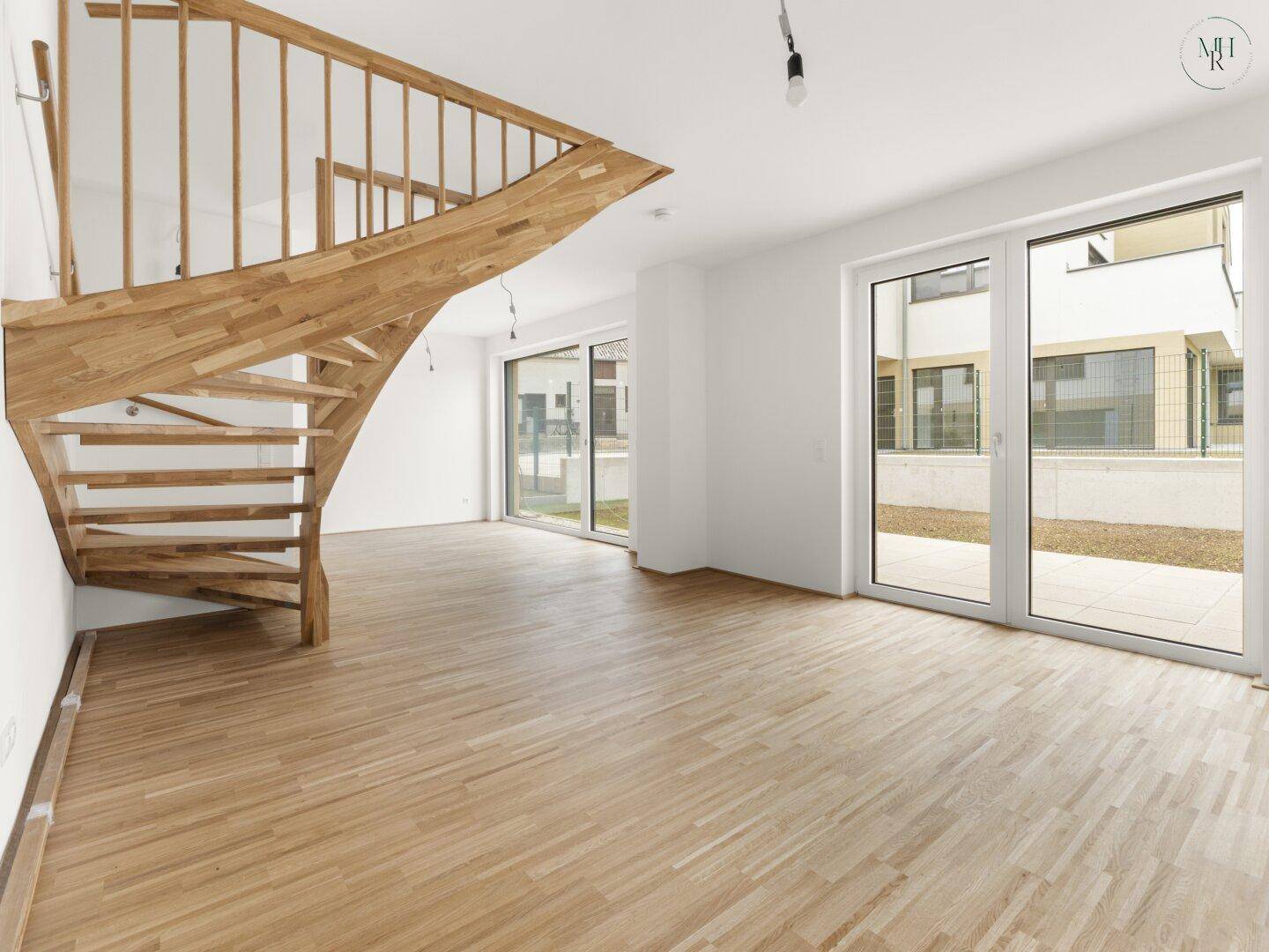 Heller Wohnbereich mit Holztreppe und Zugang zum Außenbereich durch große Fenstertüren.