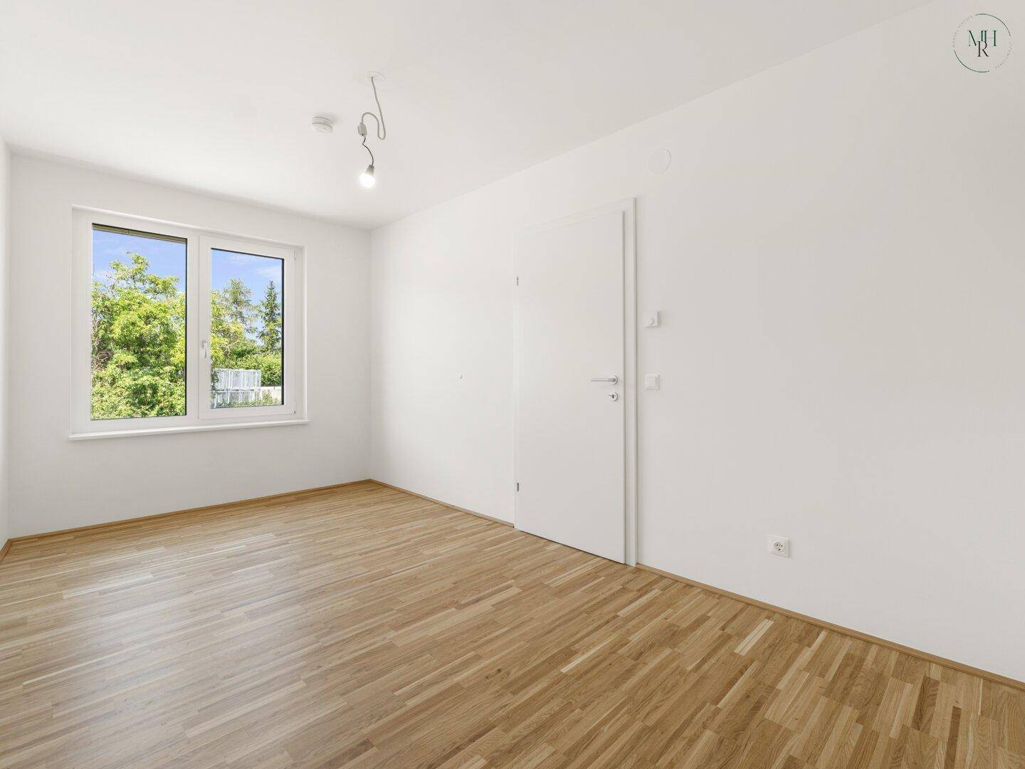 Helles Zimmer mit Holzboden und großem Fenster mit Blick ins Grüne.