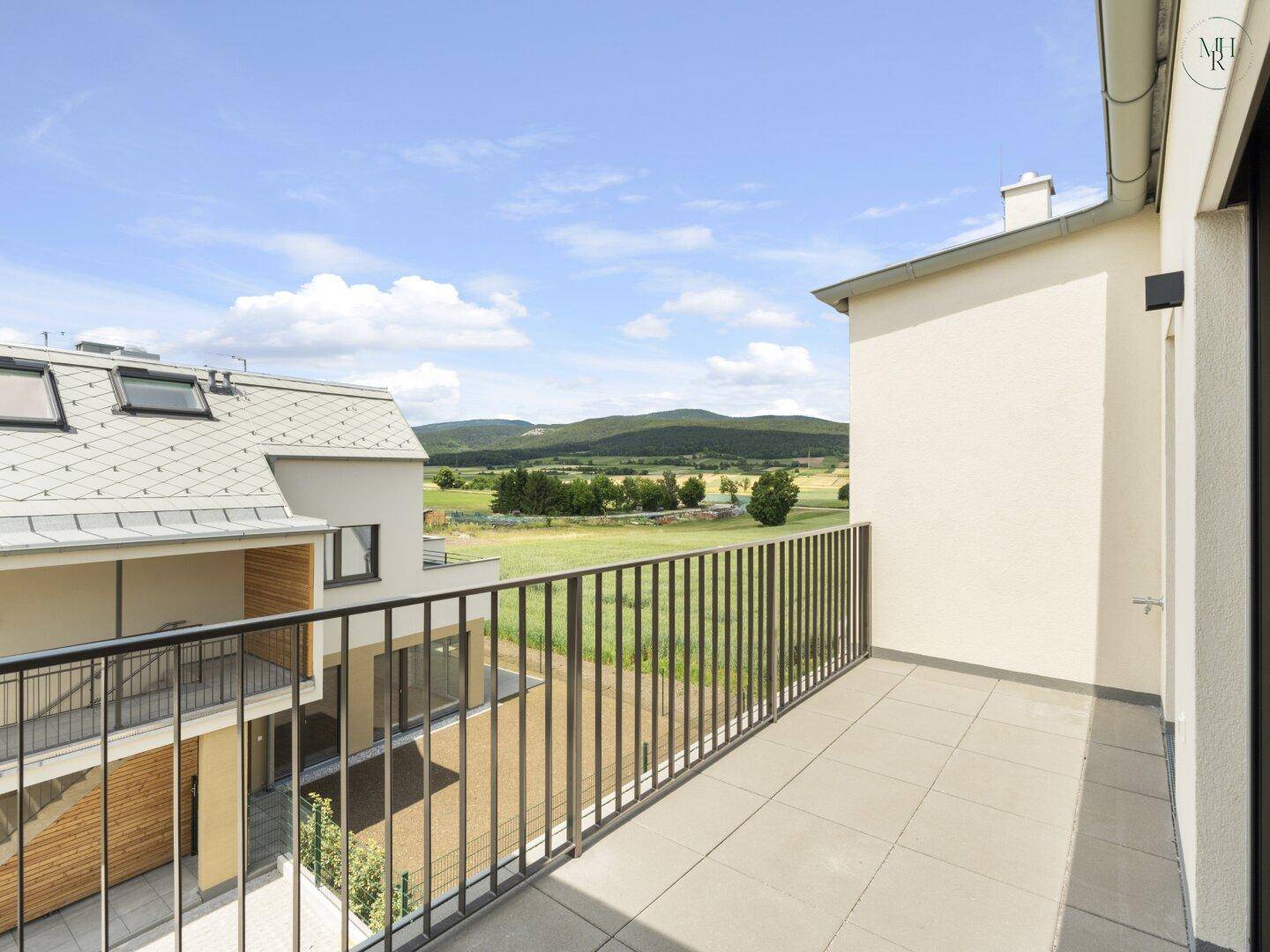Geräumiger Balkon mit Fliesenboden und weitem Blick über die grüne Landschaft und Berge.