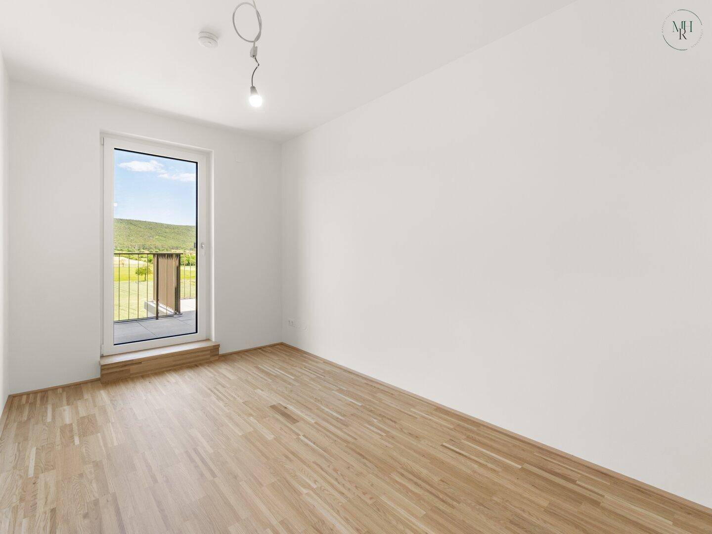 Geräumiges Schlafzimmer mit Holzboden und Zugang zu einem kleinen Balkon mit Weitblick.