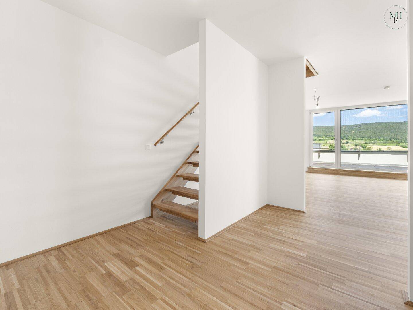 Heller Flur mit Holztreppe und Holzboden, der zu weiteren Räumen und einem großen Fenster führt.