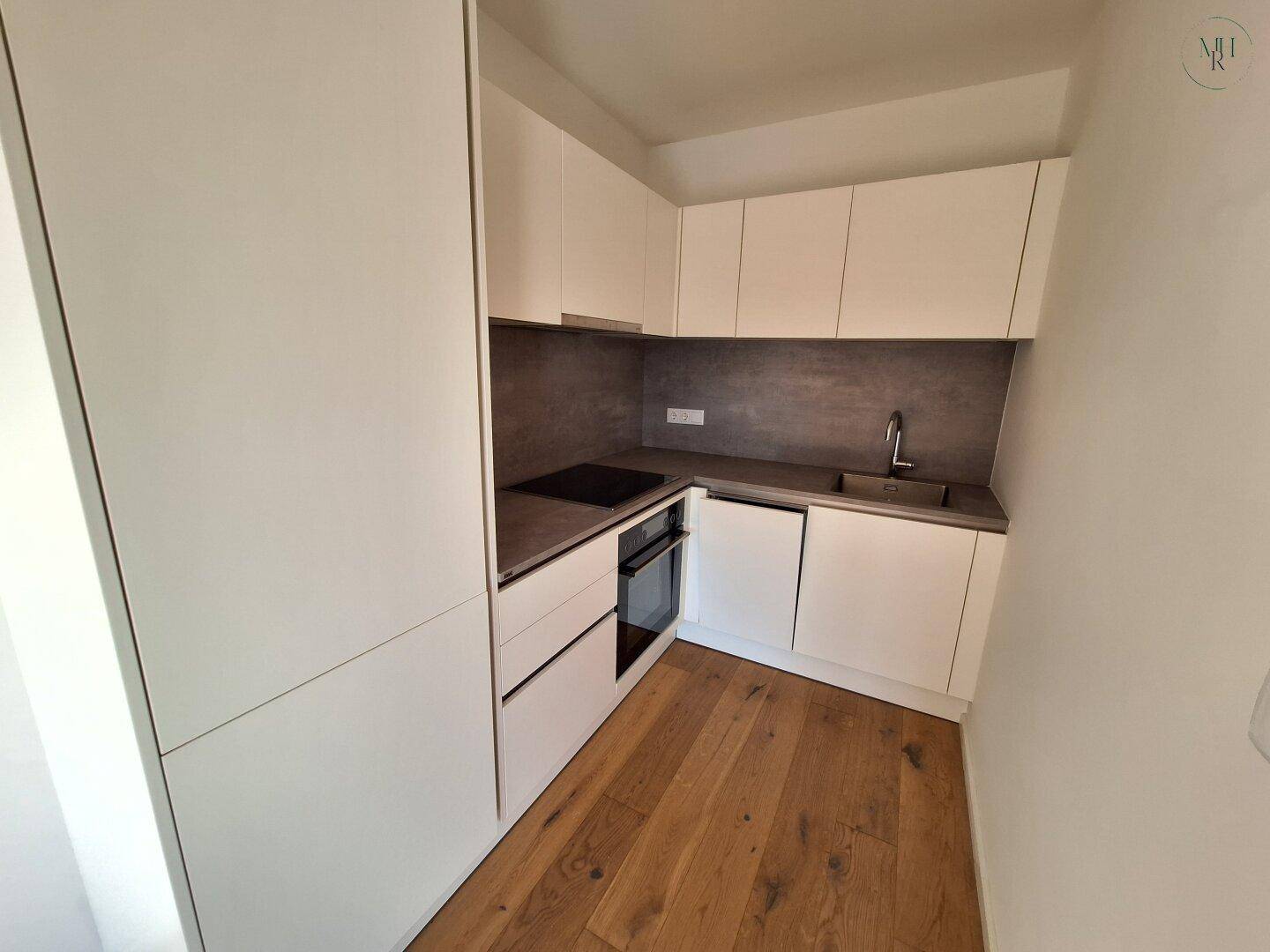 Moderne Einbauküche mit weißen Schränken, dunkler Arbeitsplatte und integrierten Geräten.