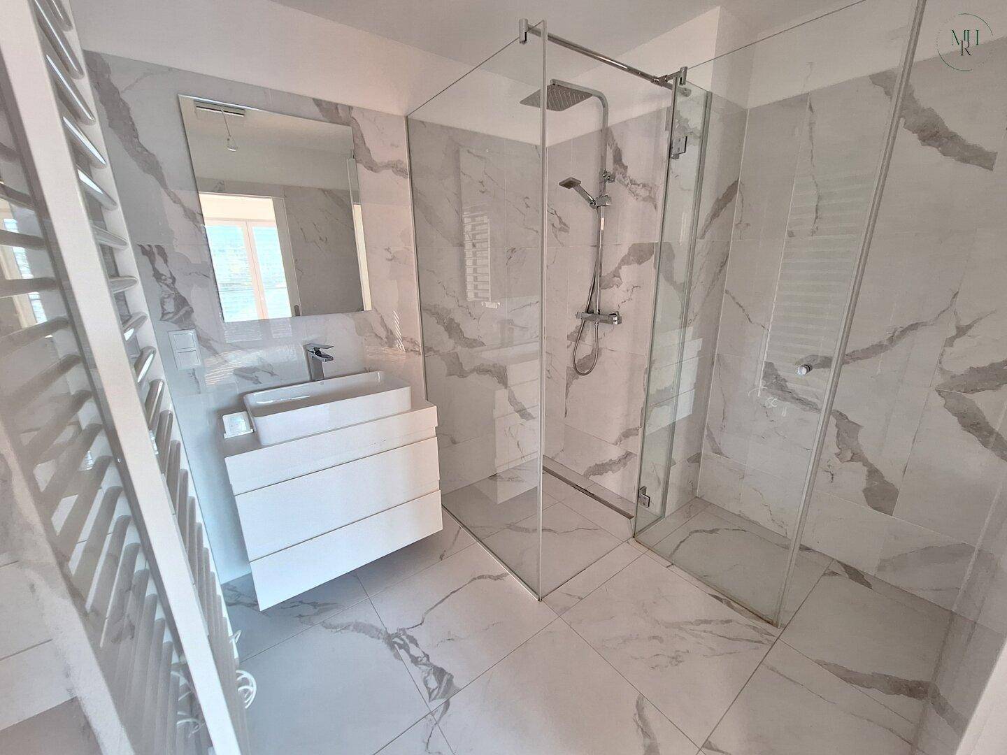 Modernes Badezimmer mit Marmorfliesen, einer begehbaren Dusche und einem beheizten Handtuchhalter.