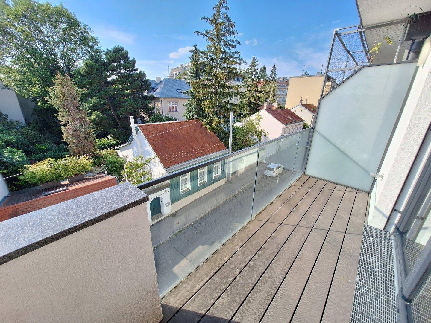 Geräumiger Balkon mit Holzdeck und Glasgeländer, bietet einen Blick auf die umliegende Nachbarschaft.