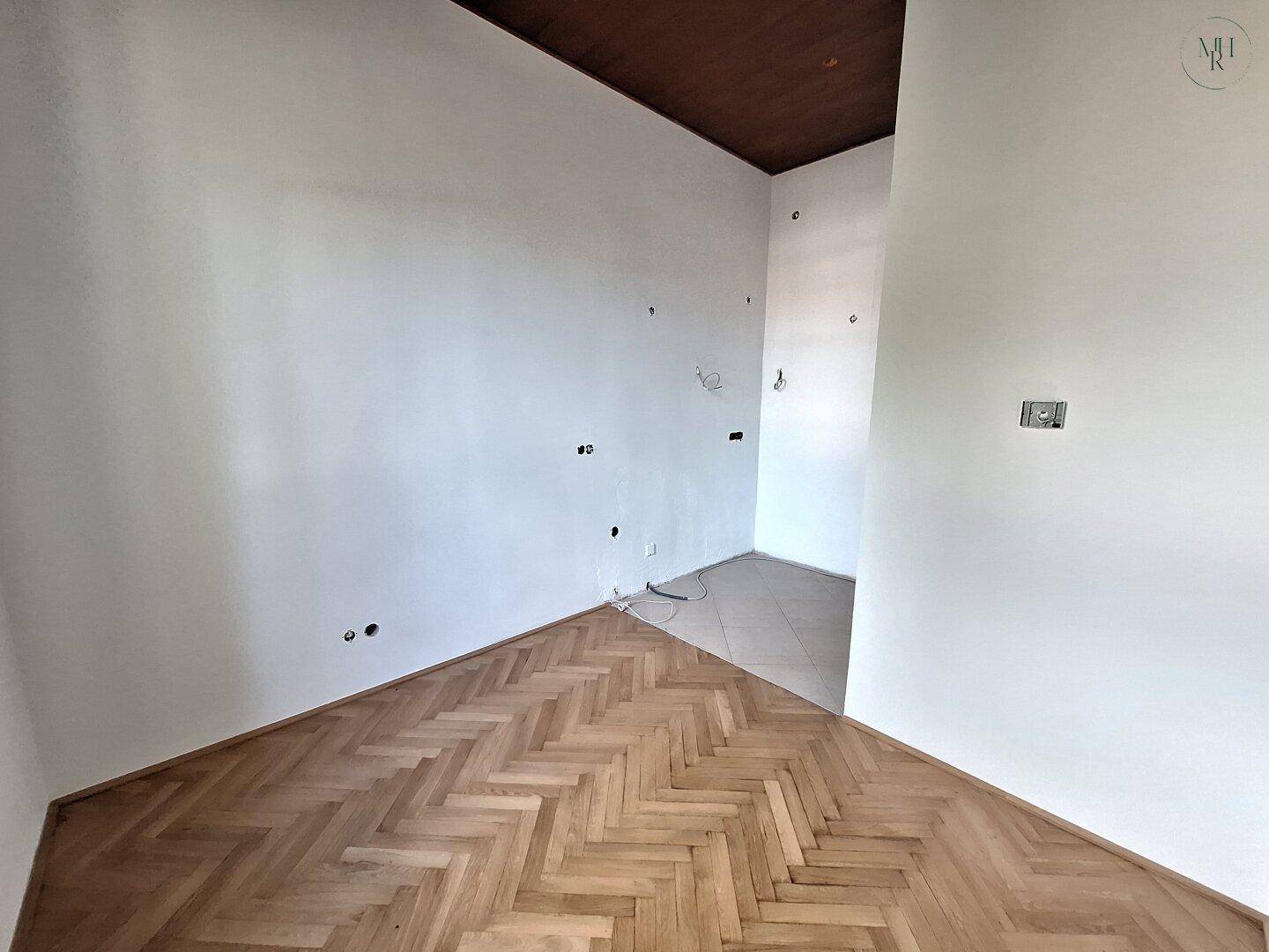 Ecke eines Raumes mit Fischgrätparkett und vorbereiteten Elektroinstallationen.