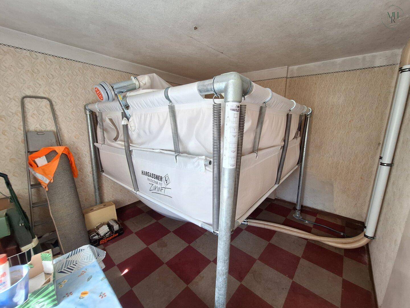 Lagerraum mit Pellet-Vorratsbehälter und kariertem Fliesenboden, der zur Heizungsanlage gehört.