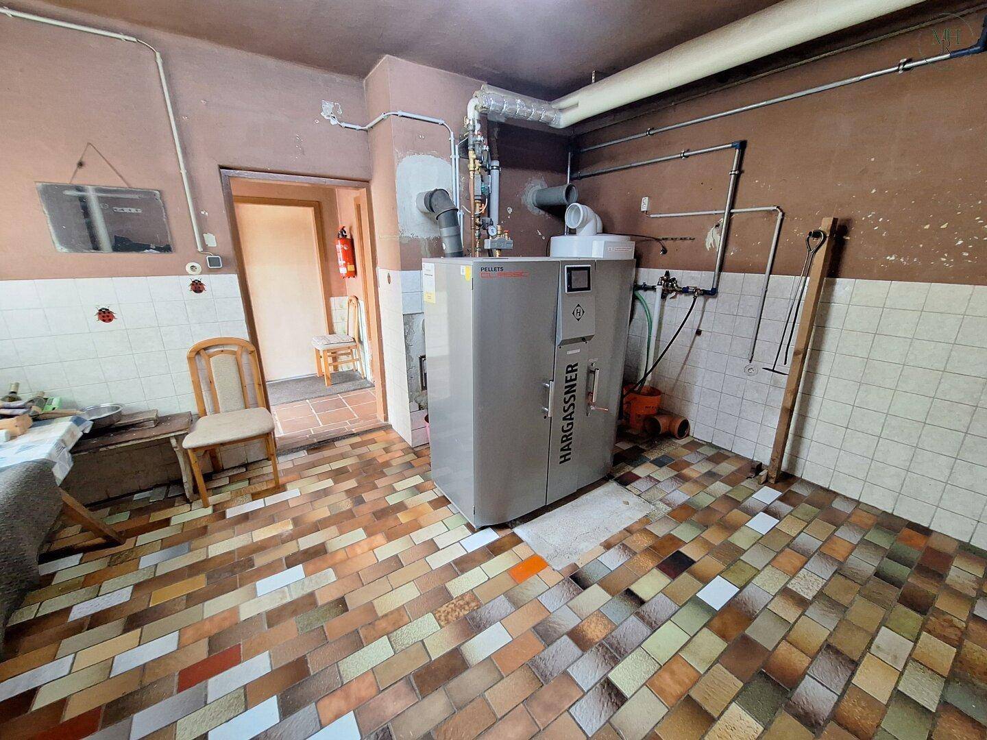 Heizungsraum mit moderner Pelletheizung und Fliesenboden, der die technische Ausstattung des Hauses zeigt.