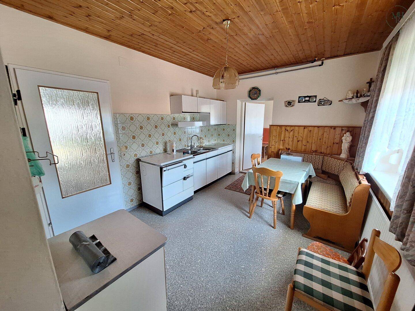 Traditionelle Küche mit Holzbalkendecke, Essbereich und älteren Einbaumöbeln im Landhausstil.