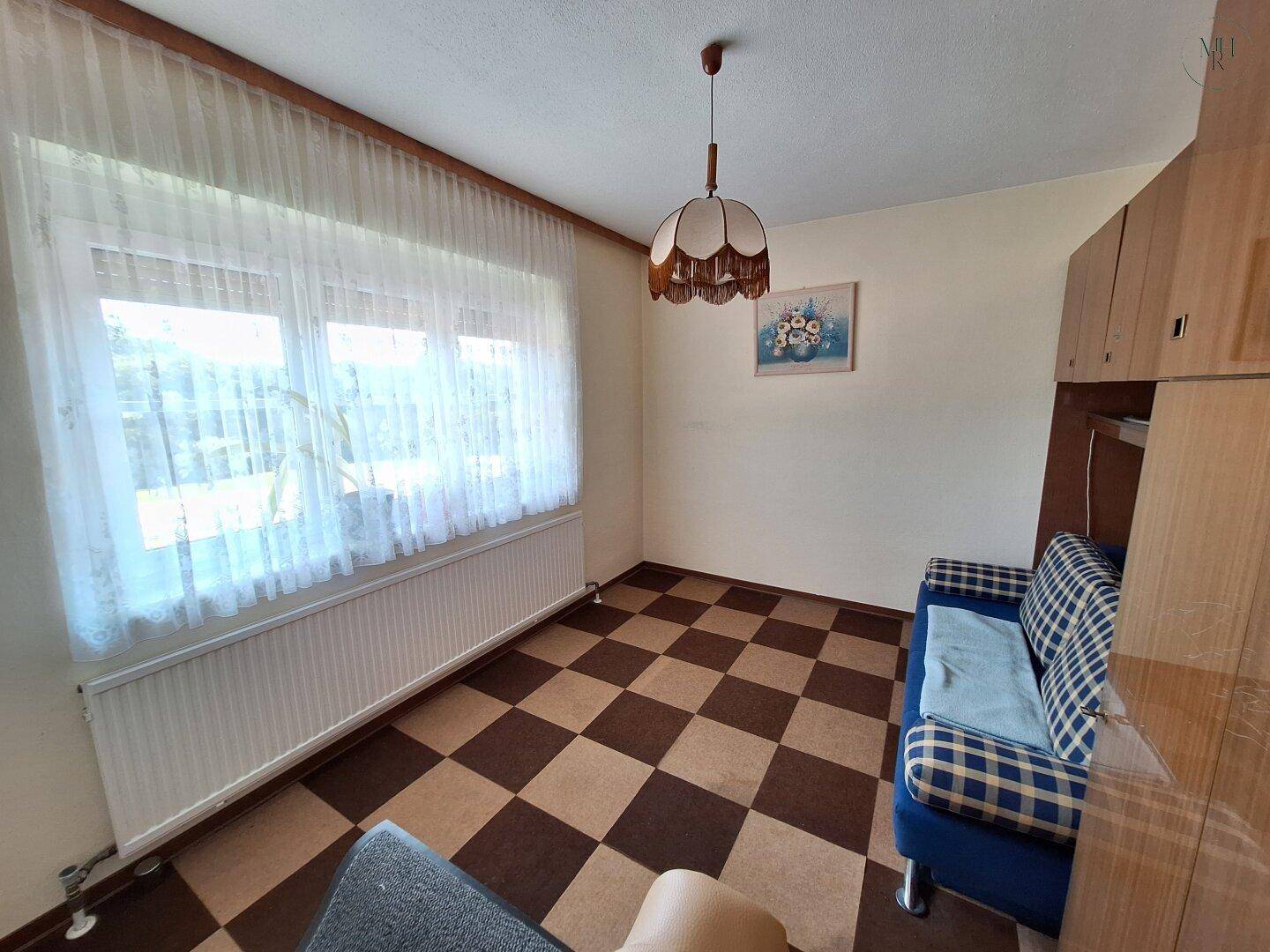 Schlafzimmer mit kariertem Teppichboden, einem Sofa und einem großen Fenster, das viel Licht hereinlässt.