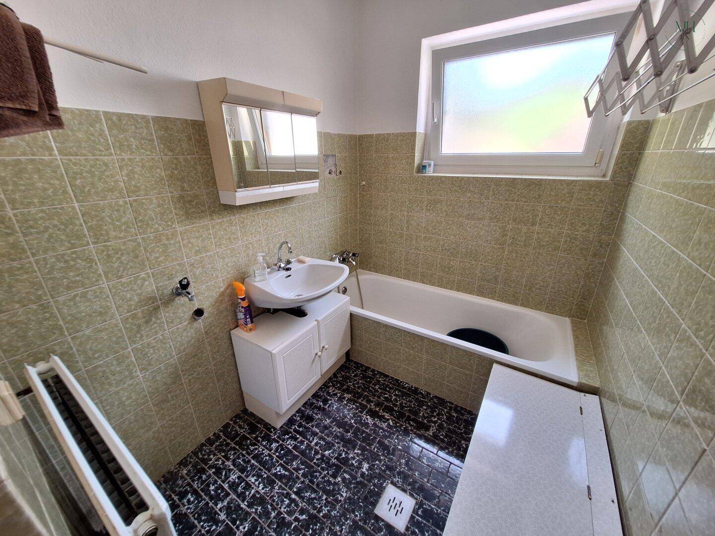 Badezimmer mit Badewanne, Waschbecken und grünen Wandfliesen im charmanten 80er-Jahre-Stil.