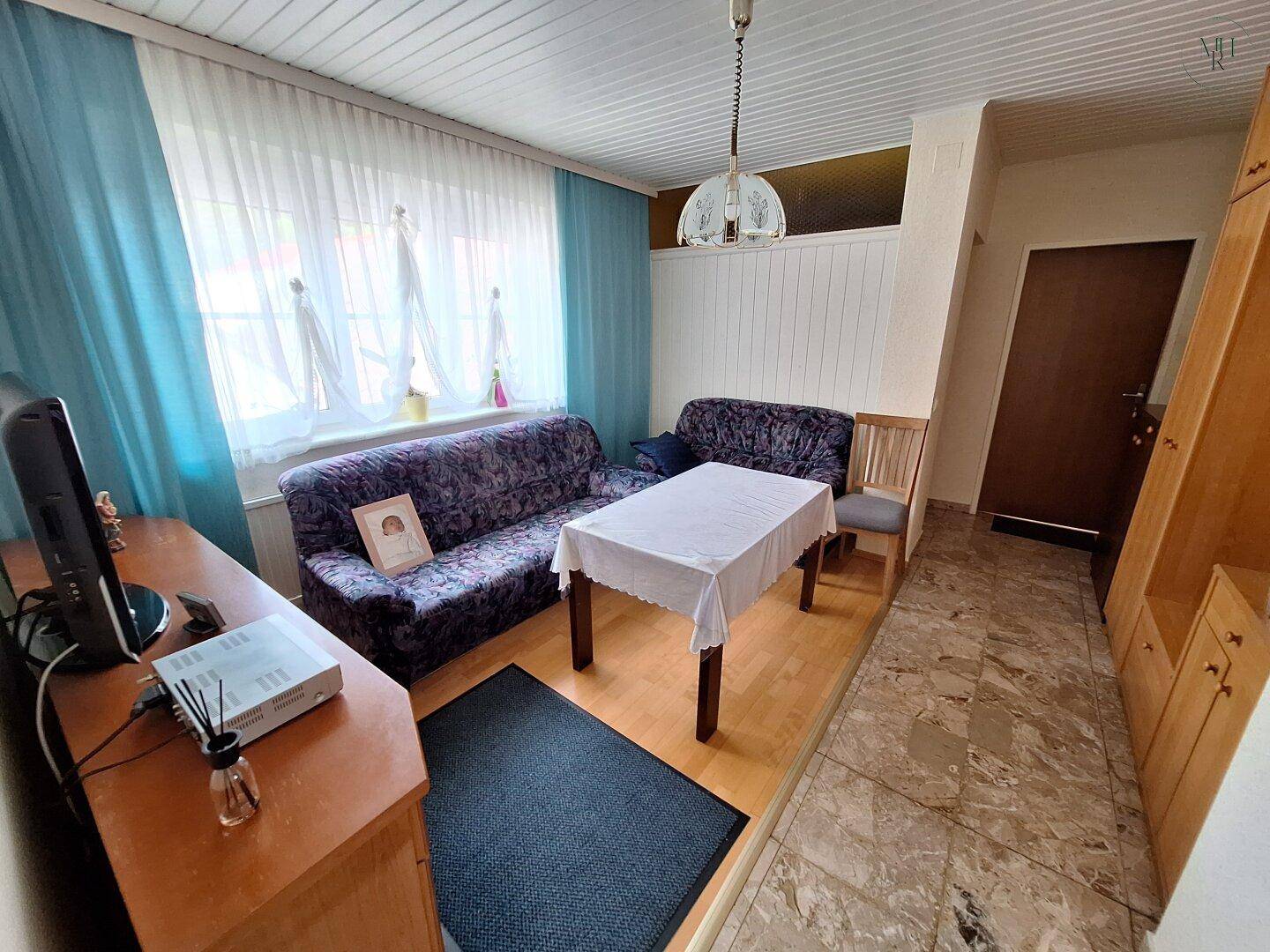 Gemütliches Wohnzimmer mit Sofa, Esstisch und einem Fenster mit blauen Vorhängen, einladend gestaltet.
