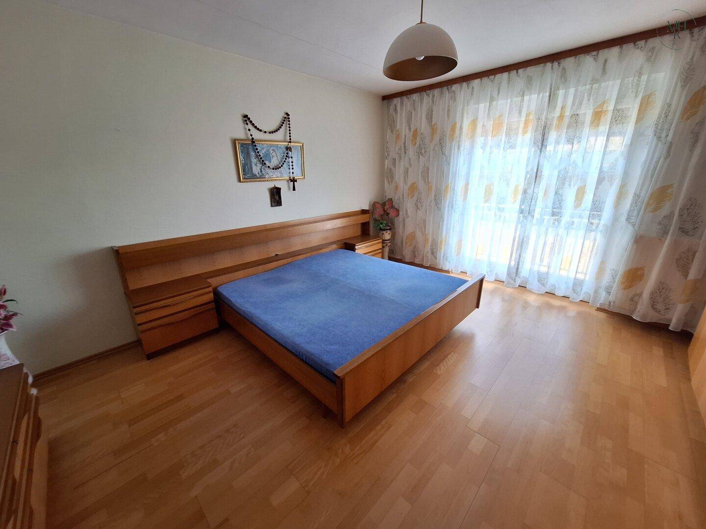 Schlafzimmer mit Holzbett, Nachttischen und einem großen Fenster mit Vorhängen, hell und geräumig.