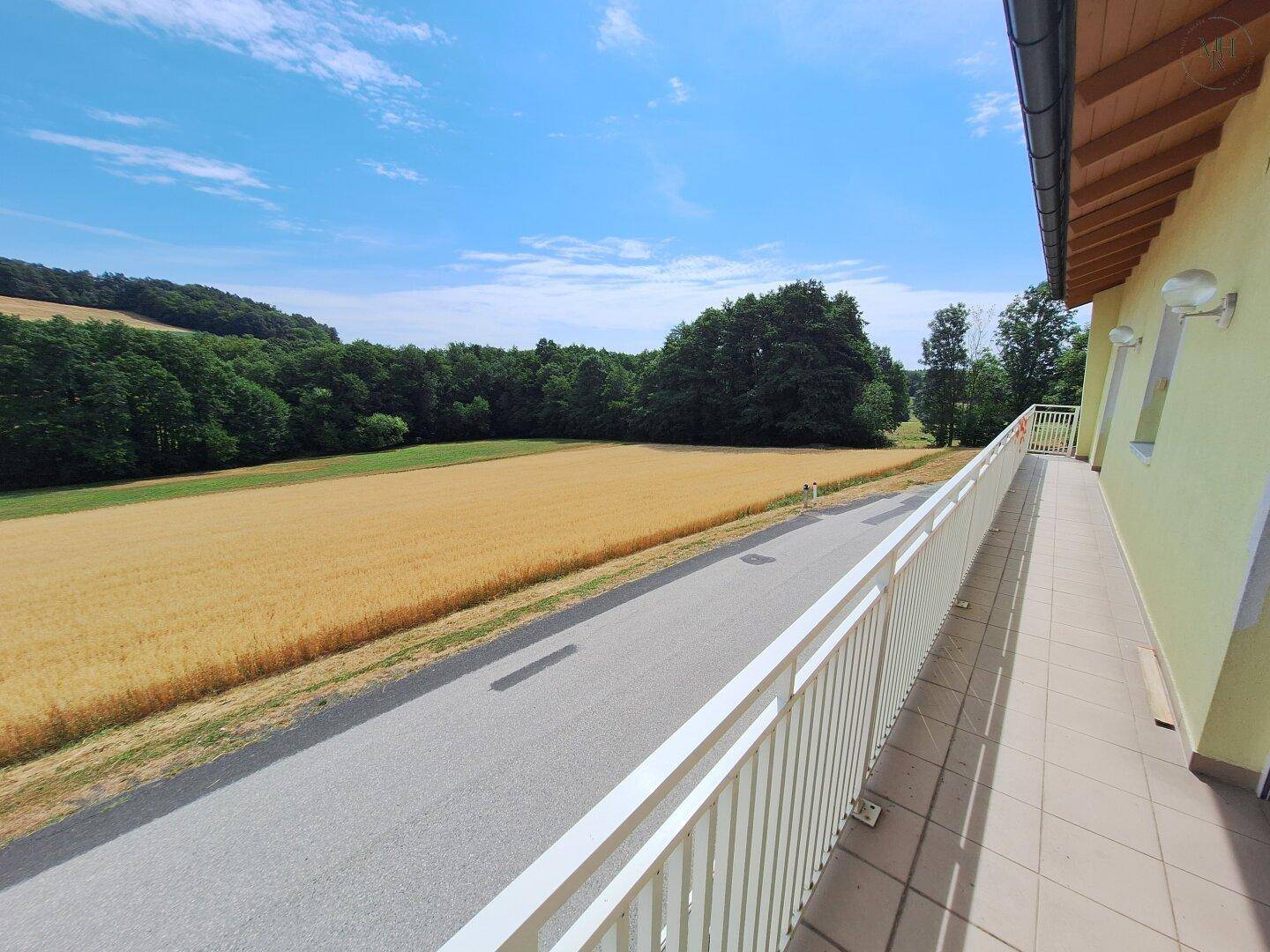 Langer Balkon mit Fliesenboden und weitem Blick über goldene Felder und grüne Wälder.
