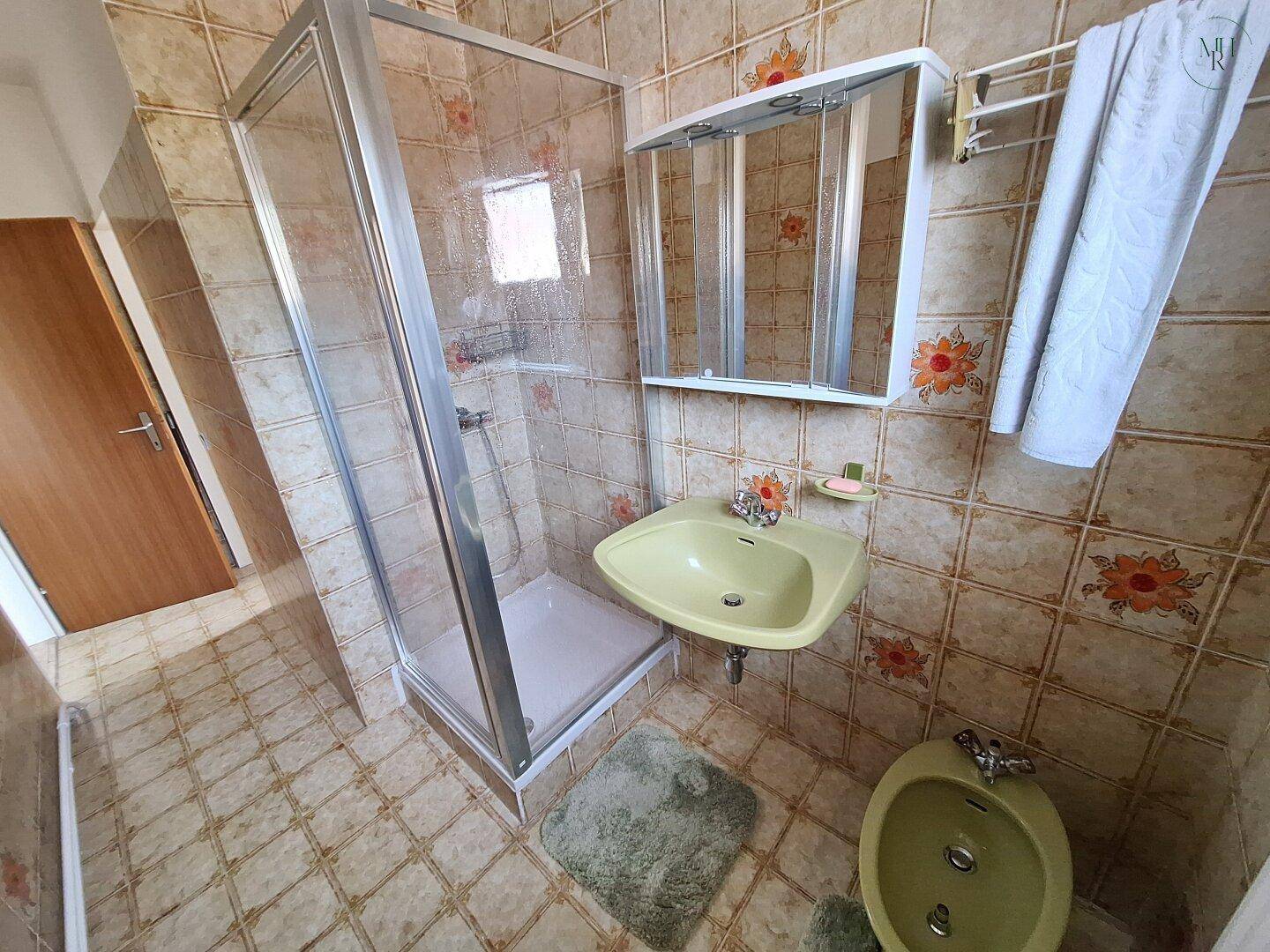 Badezimmer mit Duschkabine, Waschbecken und Bidet, dekoriert mit floralen Fliesen und Spiegelschrank.