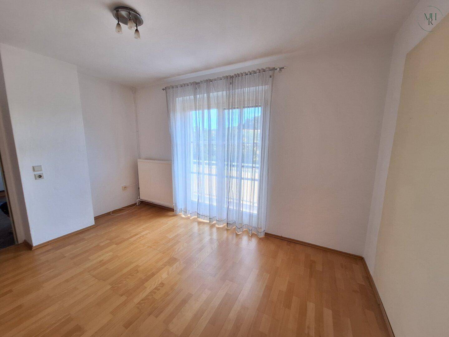 Helles Zimmer mit Parkettboden und einem großen Fenster, das viel Licht hereinlässt, vielseitig nutzbar.