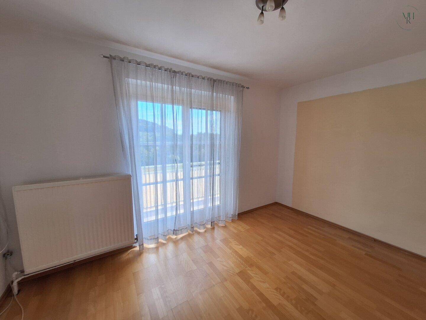 Geräumiges Zimmer mit Holzboden und einem großen Fenster mit Blick ins Grüne, hell und einladend.