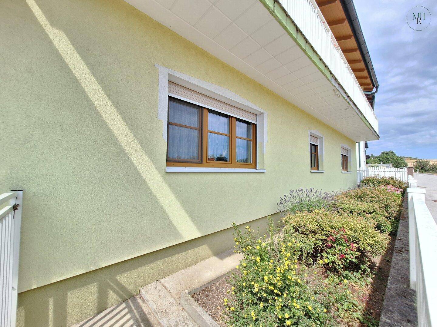Seitenansicht eines gelben Hauses mit Fenstern und einem kleinen Gartenbereich, gut gepflegt.