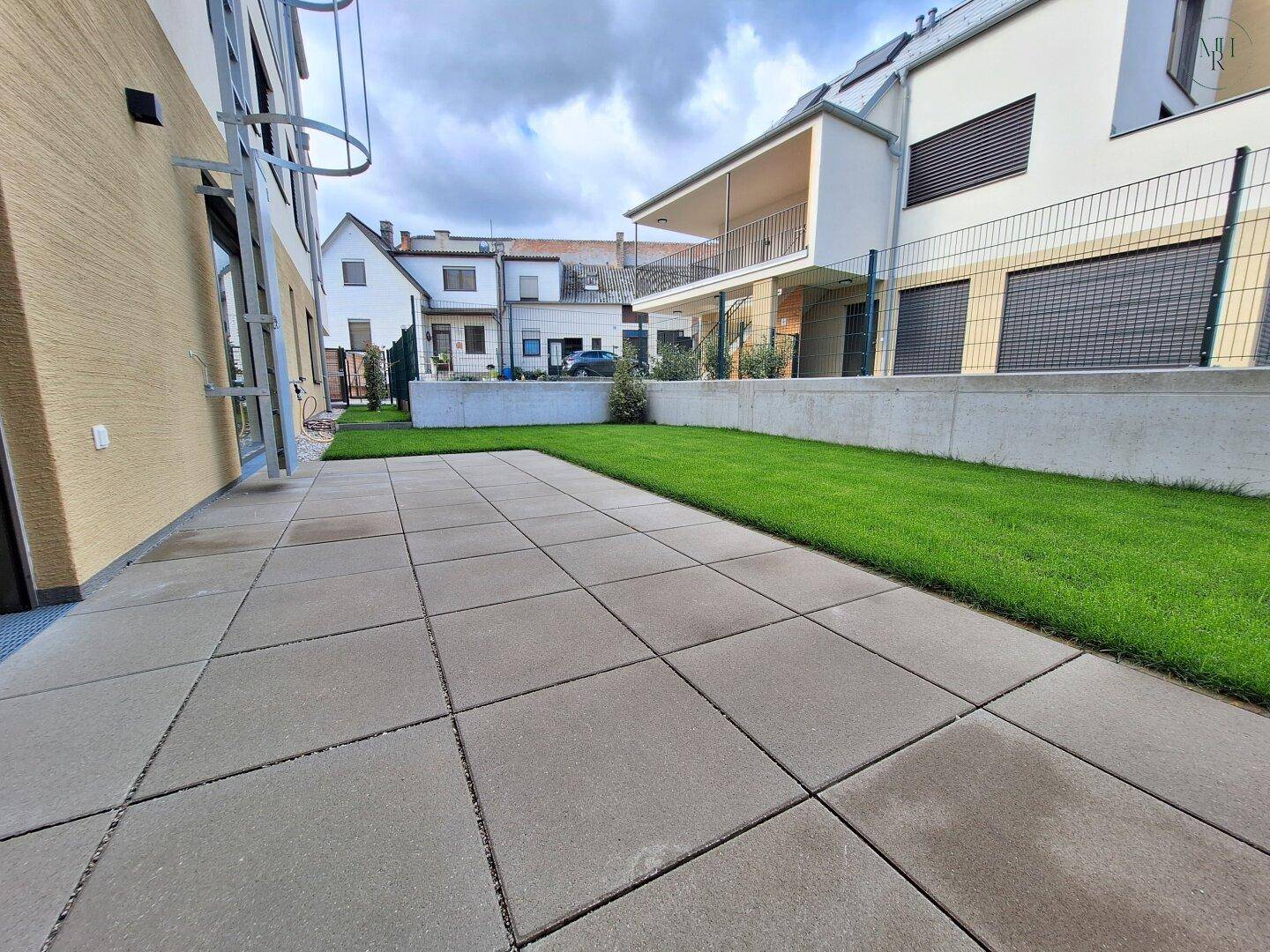 Großzügige gepflasterte Terrasse mit angrenzendem Rasenbereich am modernen Gebäude.