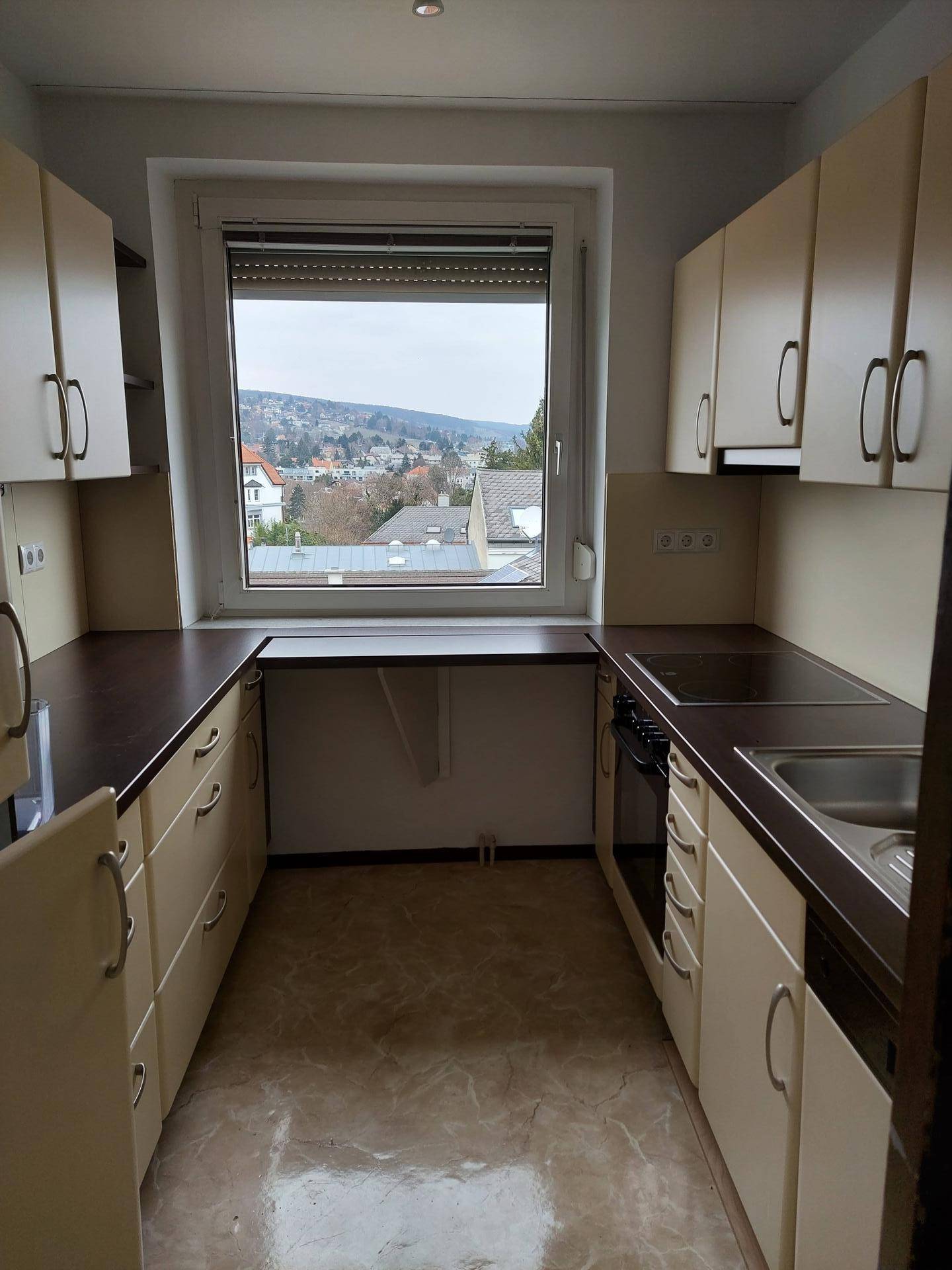 Funktionale Küche mit beigen Schränken, dunklen Arbeitsplatten und Fenster mit Ausblick.