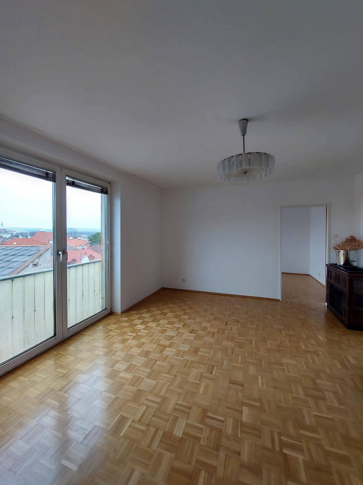Helles, leeres Wohnzimmer mit Fischgrätparkett, weißen Wänden und Zugang zum Balkon.