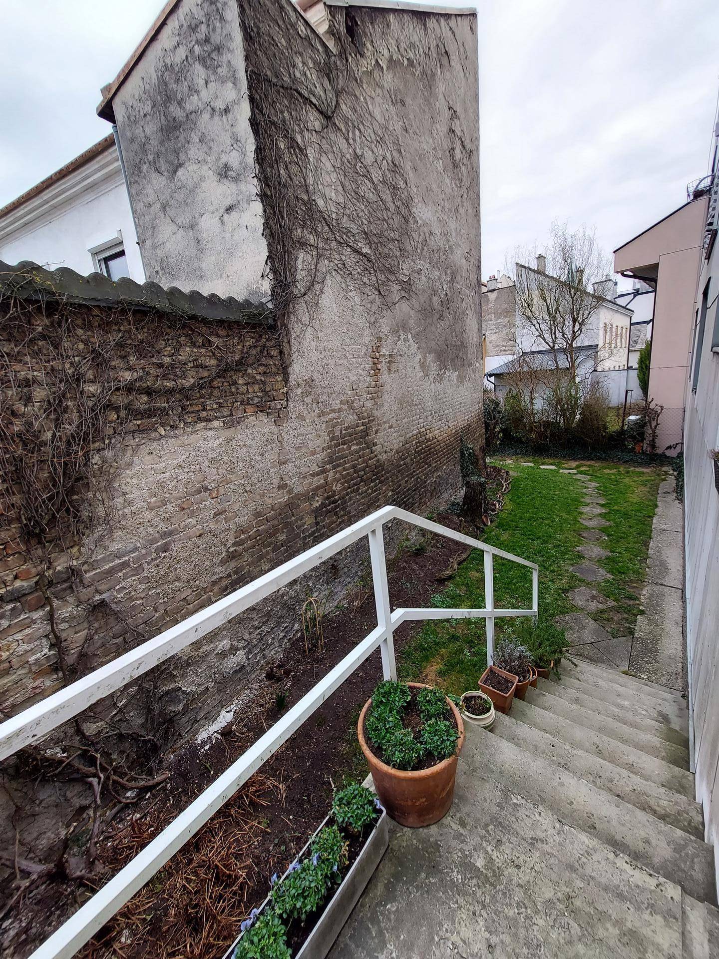 Schmaler Gartenbereich mit Steintreppe, alten Ziegelmauern und etwas Grün.