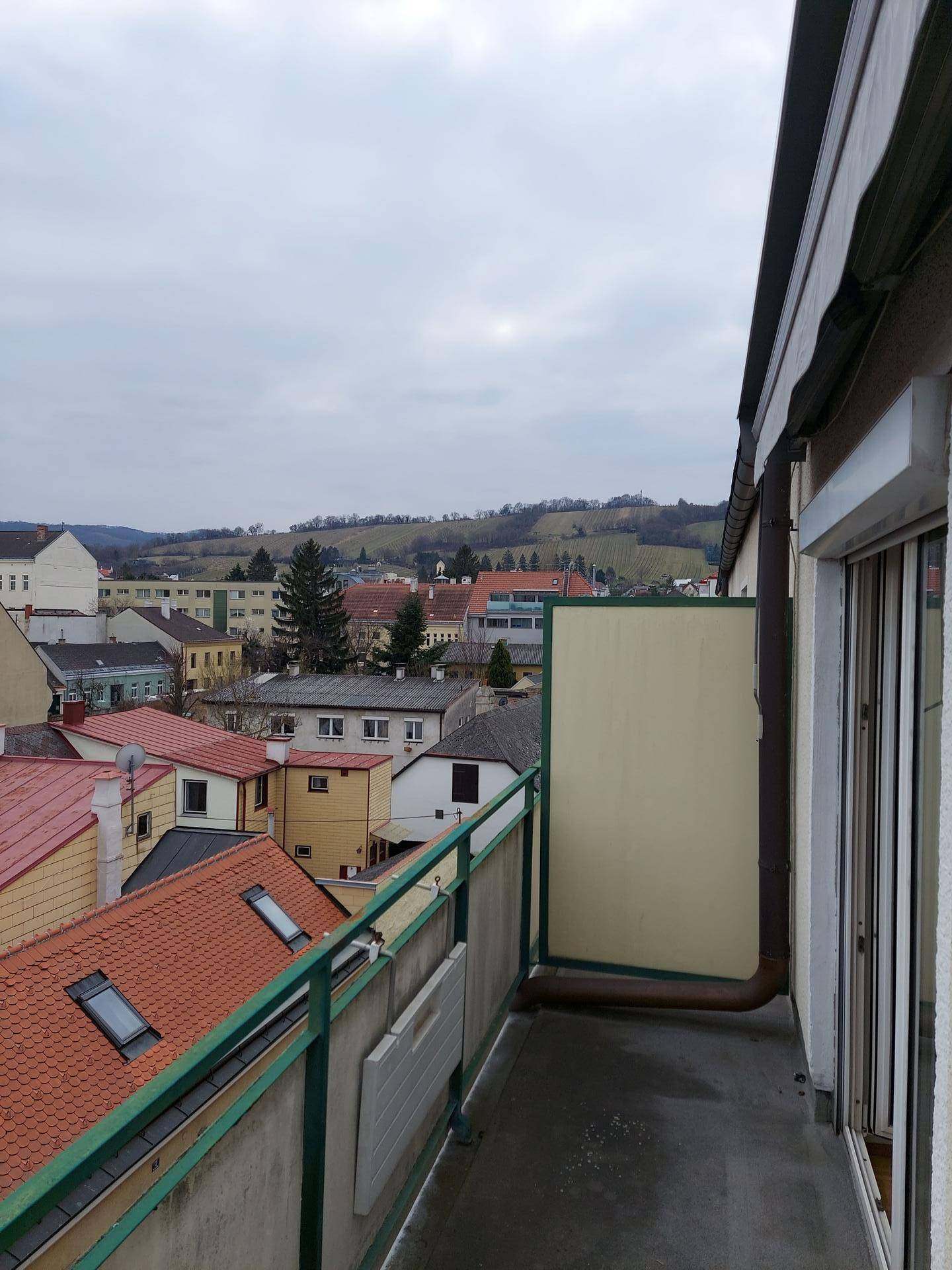 Schmaler Balkon mit grüner Brüstung und Blick über die Dächer und sanften Hügel.