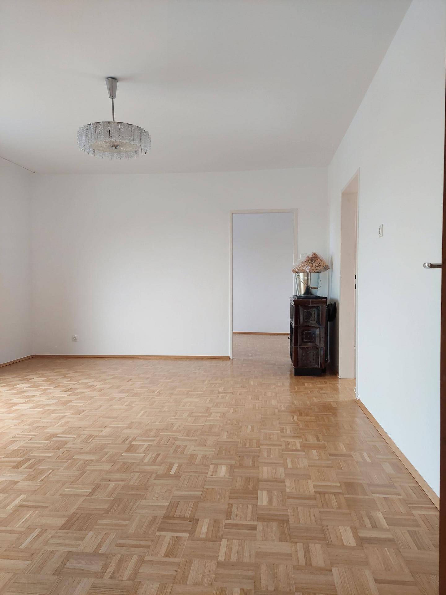 Geräumiges, helles Wohnzimmer mit Parkettboden, schlichten weißen Wänden und Kronleuchter.