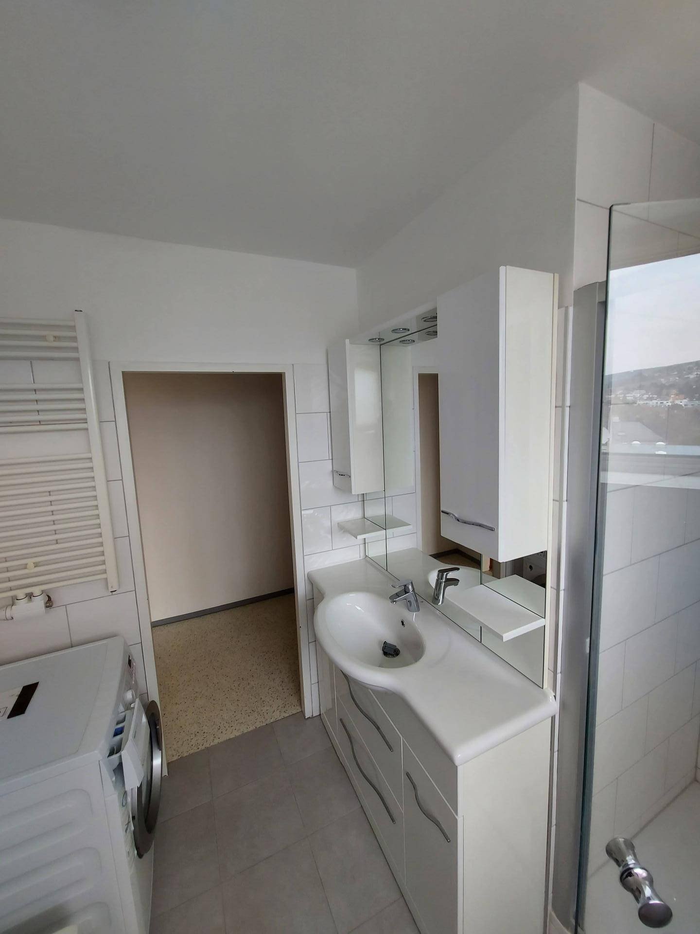 Modernes Badezimmer mit Waschbecken, Spiegelschrank, Duschkabine und Waschmaschine.