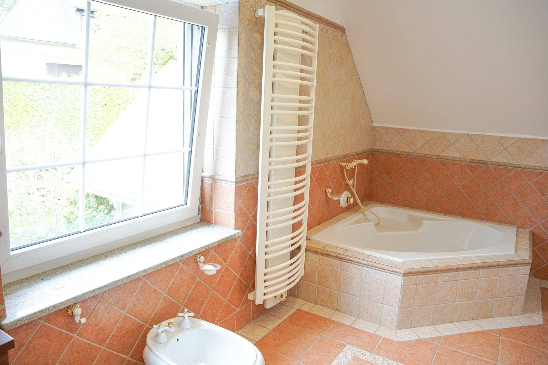 Badezimmer mit Eckbadewanne, Bidet, Fenster und Handtuchheizkörper.