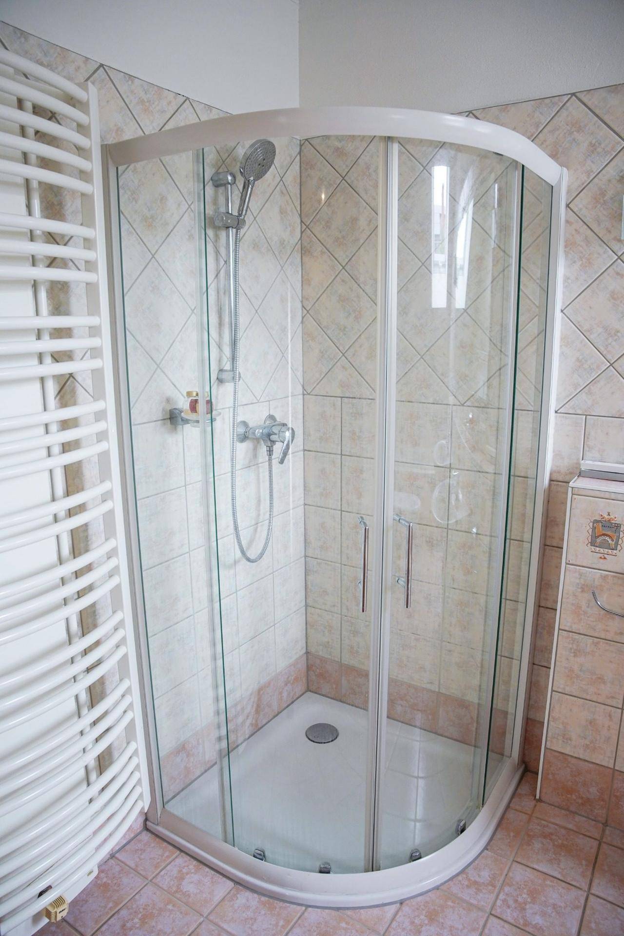 Badezimmer mit Eckduschkabine, beigefarbenen Fliesen und Handtuchheizkörper.
