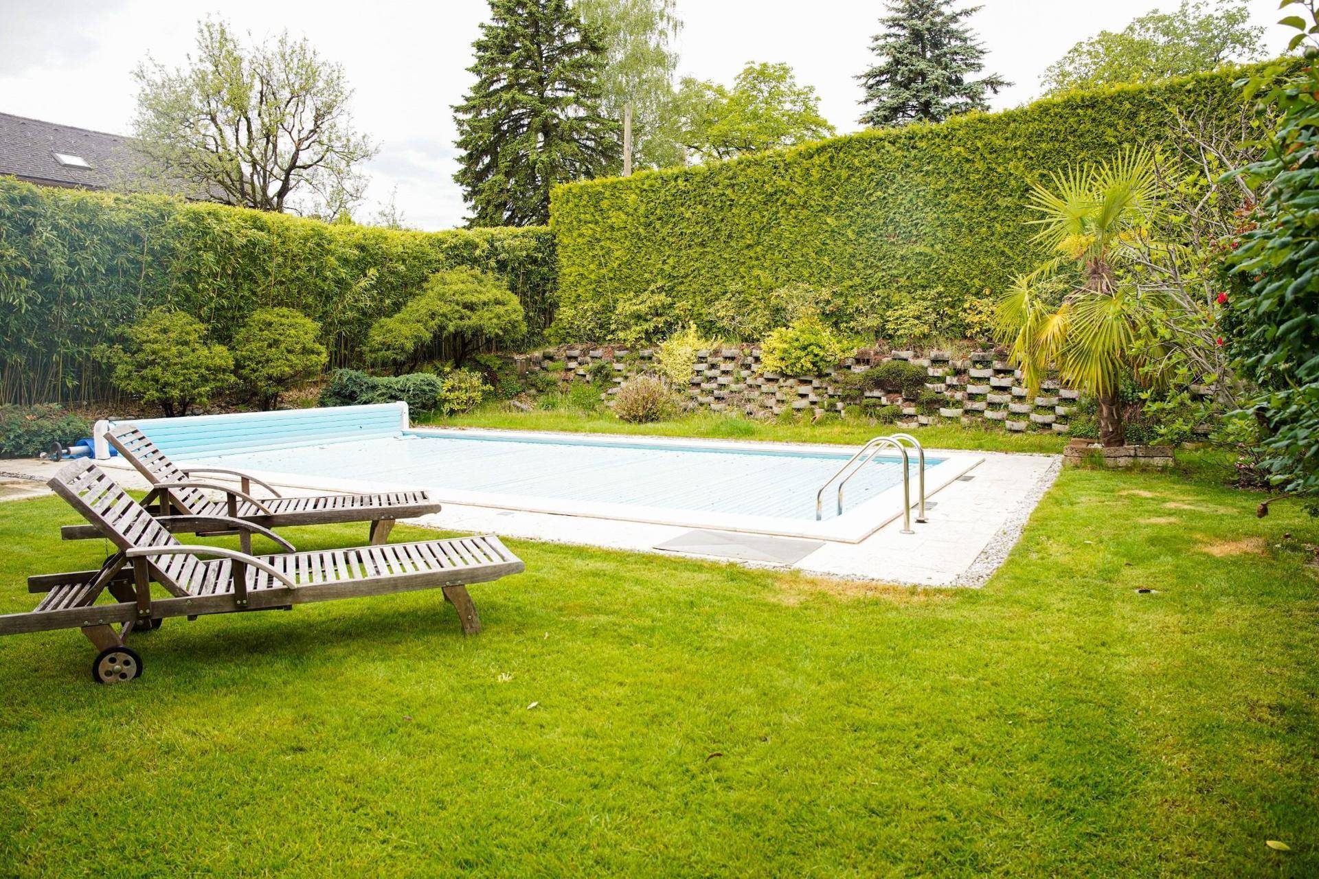 Großzügiger Garten mit Swimmingpool, Liegestühlen und einer hohen Hecke als Sichtschutz.