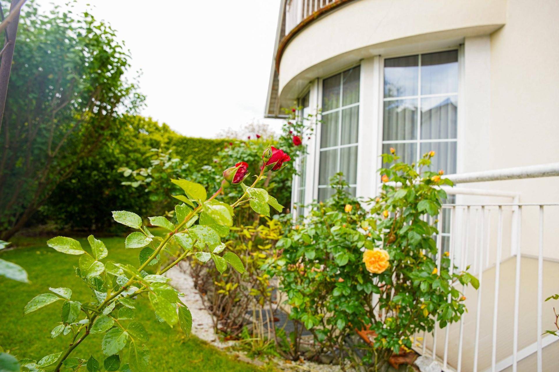 Detailaufnahme des Gartens mit blühenden Rosen und einem kleinen Balkon am Haus.