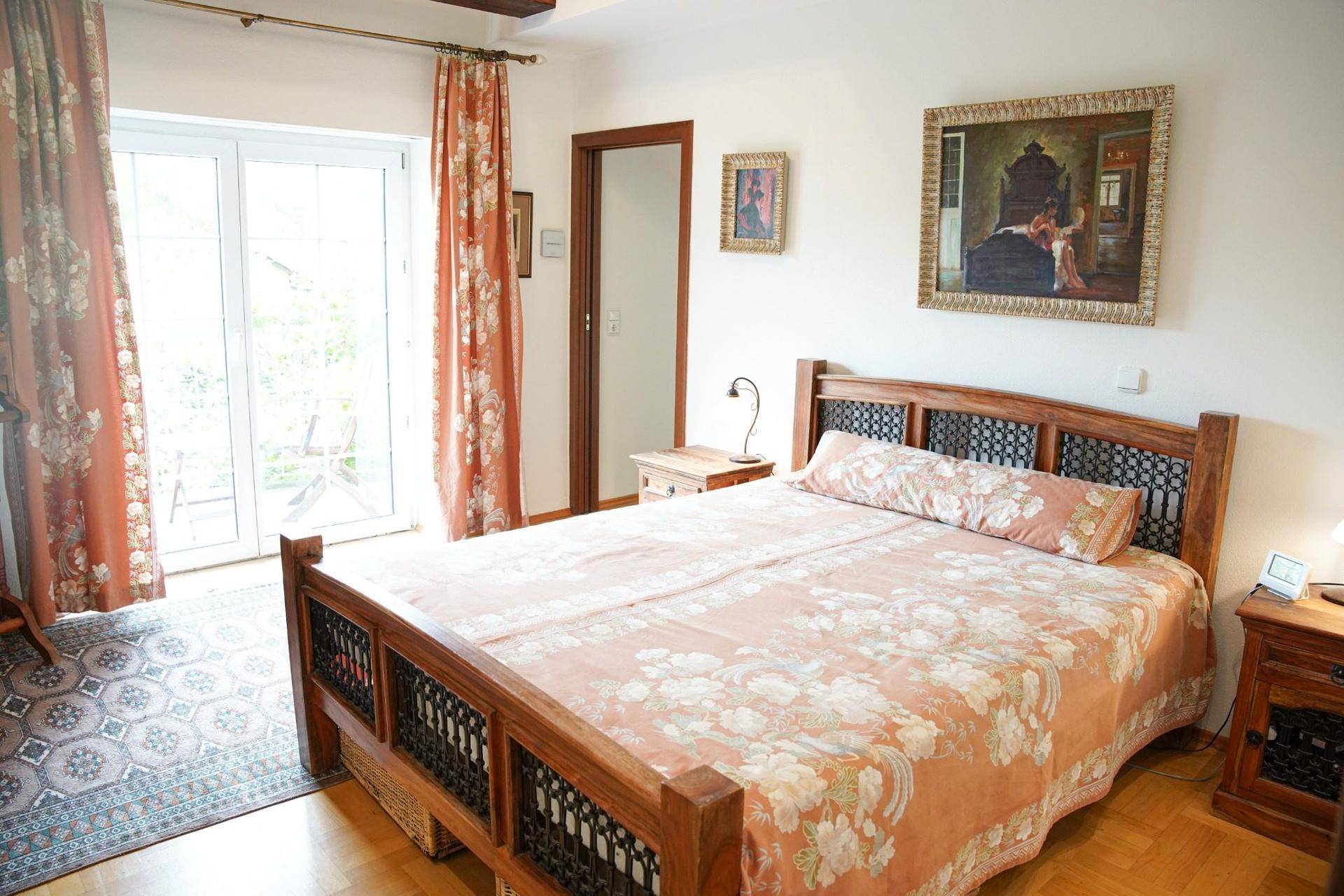 Helles Schlafzimmer mit Holzbett, Parkettboden und Zugang zu einem Balkon oder einer Terrasse.