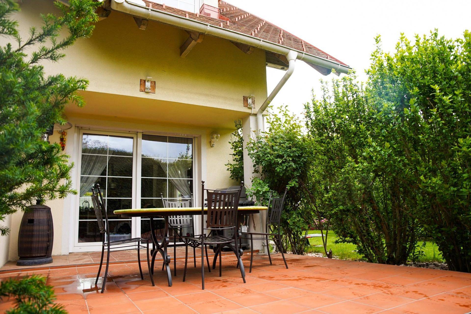 Gemütliche Terrasse mit Terrakotta-Fliesen und einem Esstisch, umgeben von grünen Büschen.