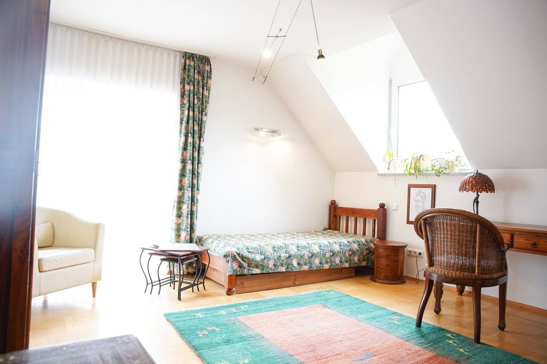 Helles Schlafzimmer im Dachgeschoss mit Einzelbett, Schreibtisch und schrägen Wänden.