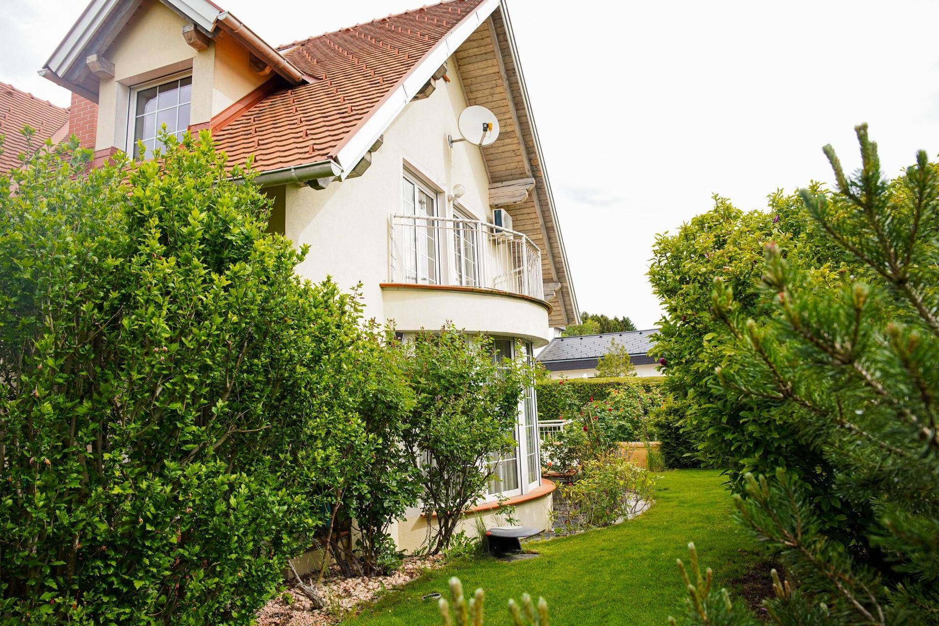 Seitenansicht des Hauses mit Balkon, gepflegtem Rasen und üppigen Sträuchern.
