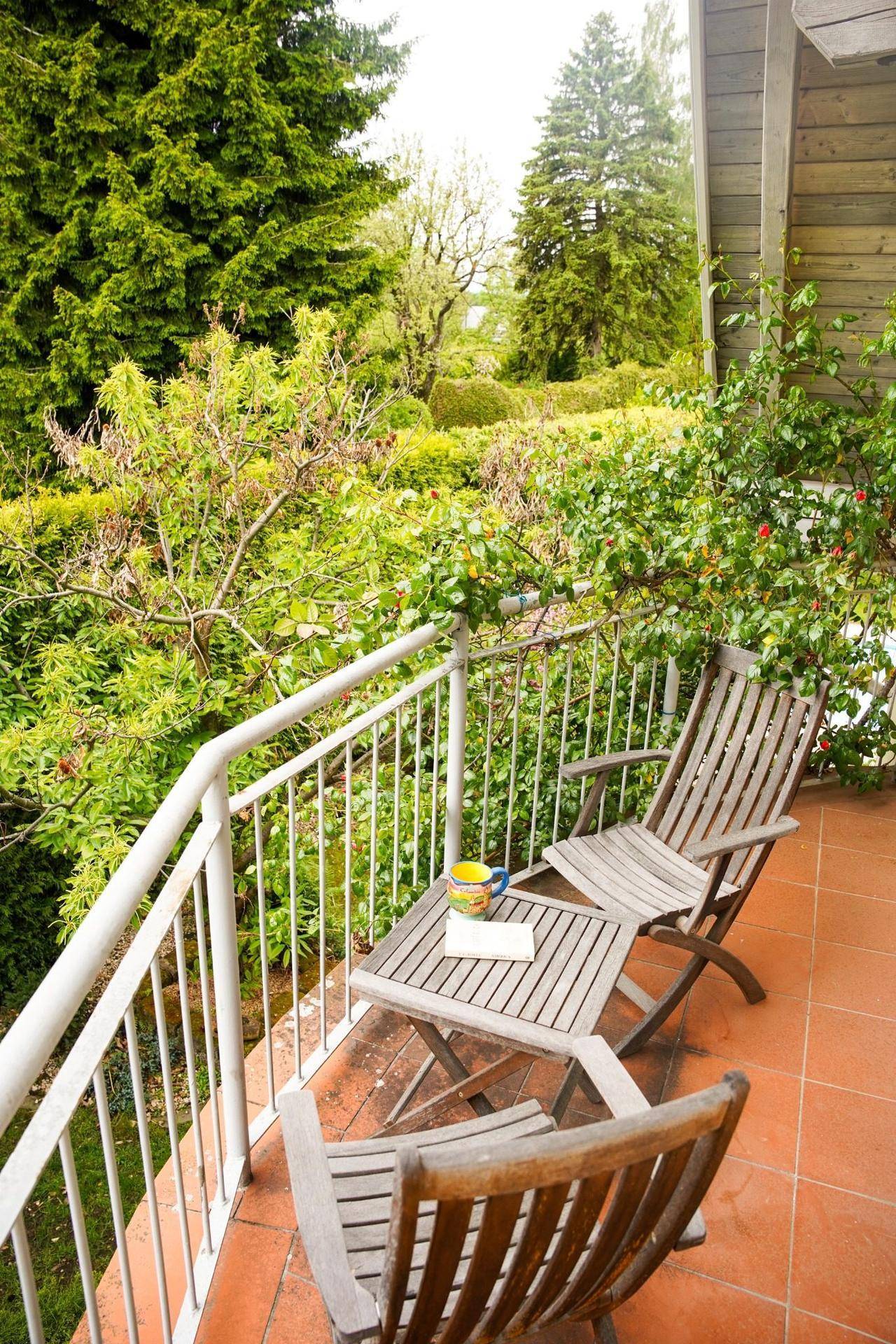 Gemütlicher Balkon mit Holztisch und Stühlen, umgeben von üppigem Grün und Bäumen.