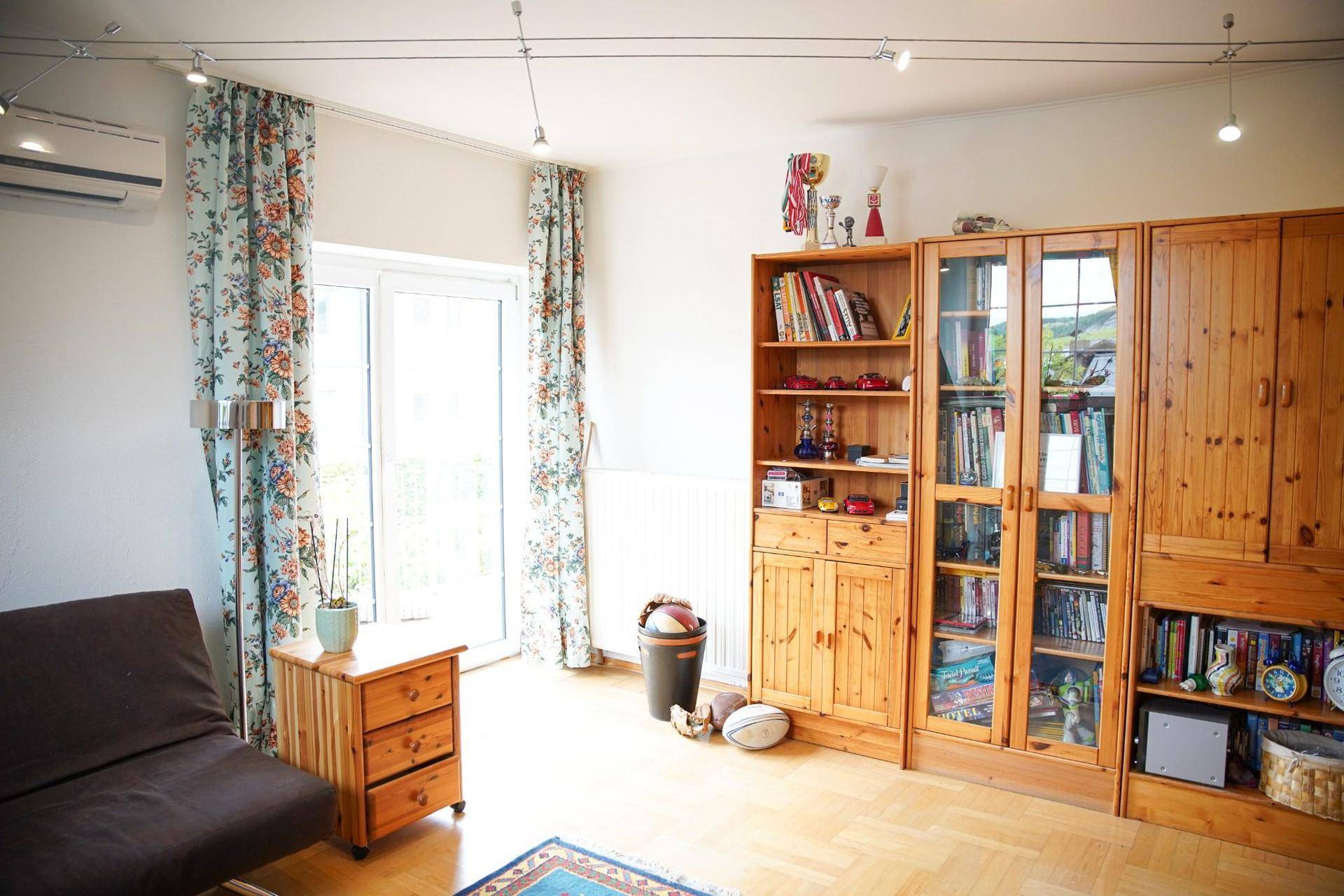 Wohnbereich mit Holzregalen, Sofa und Zugang zu einem Balkon oder einer Terrasse.