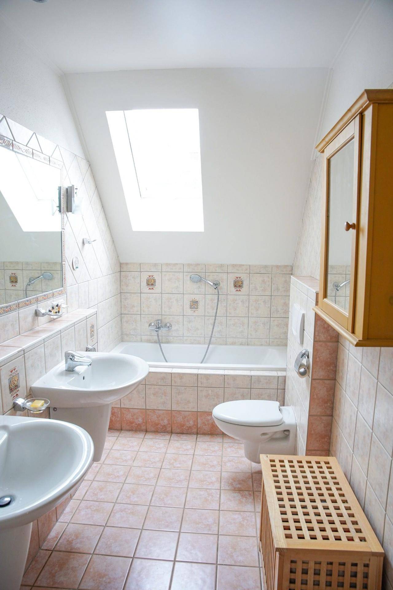 Dachgeschoss-Badezimmer mit Badewanne, zwei Waschbecken, WC und Dachfenster.