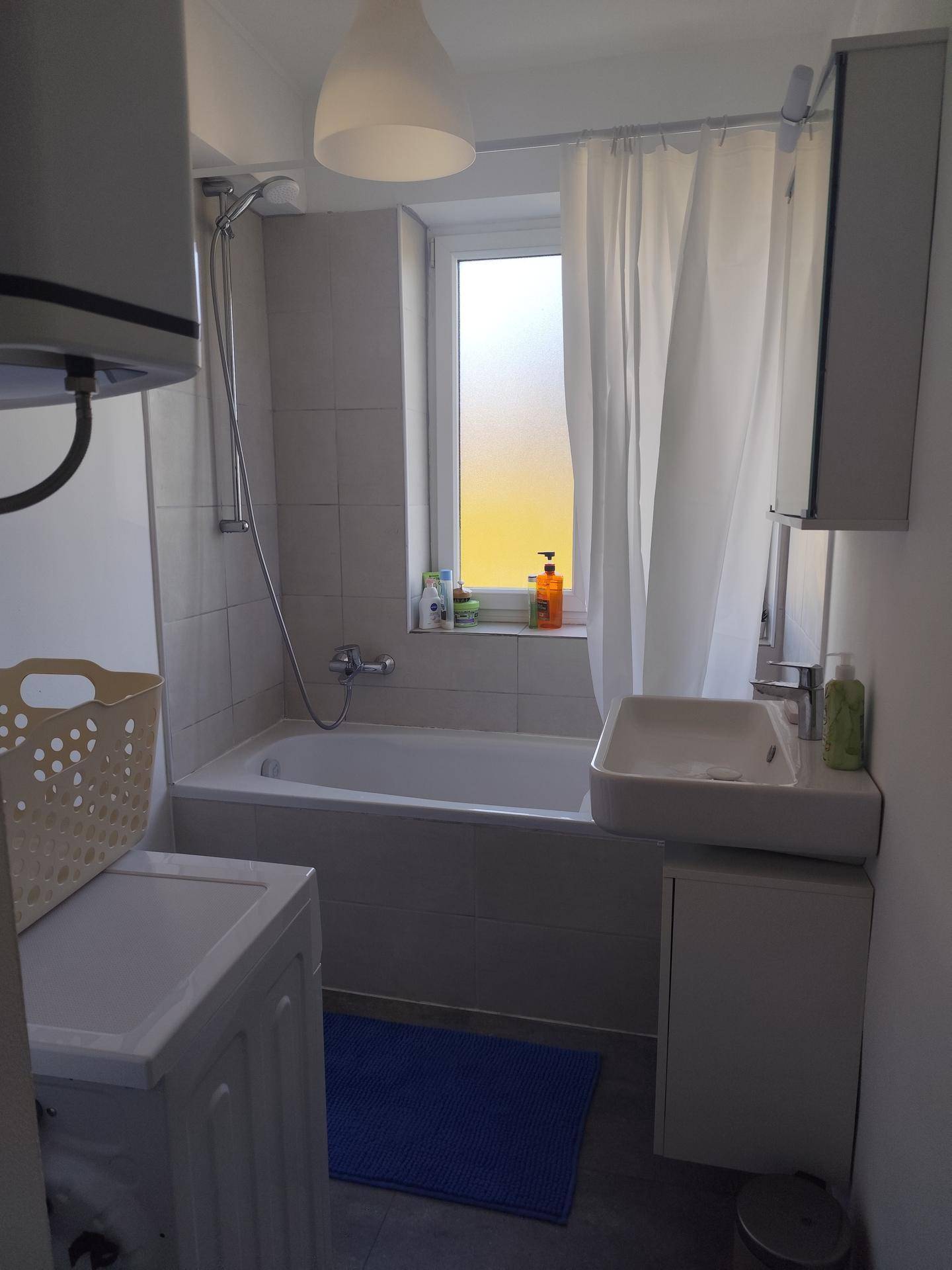 Helles Badezimmer mit Badewanne, Dusche, Waschbecken und Waschmaschine, inklusive Fenster.