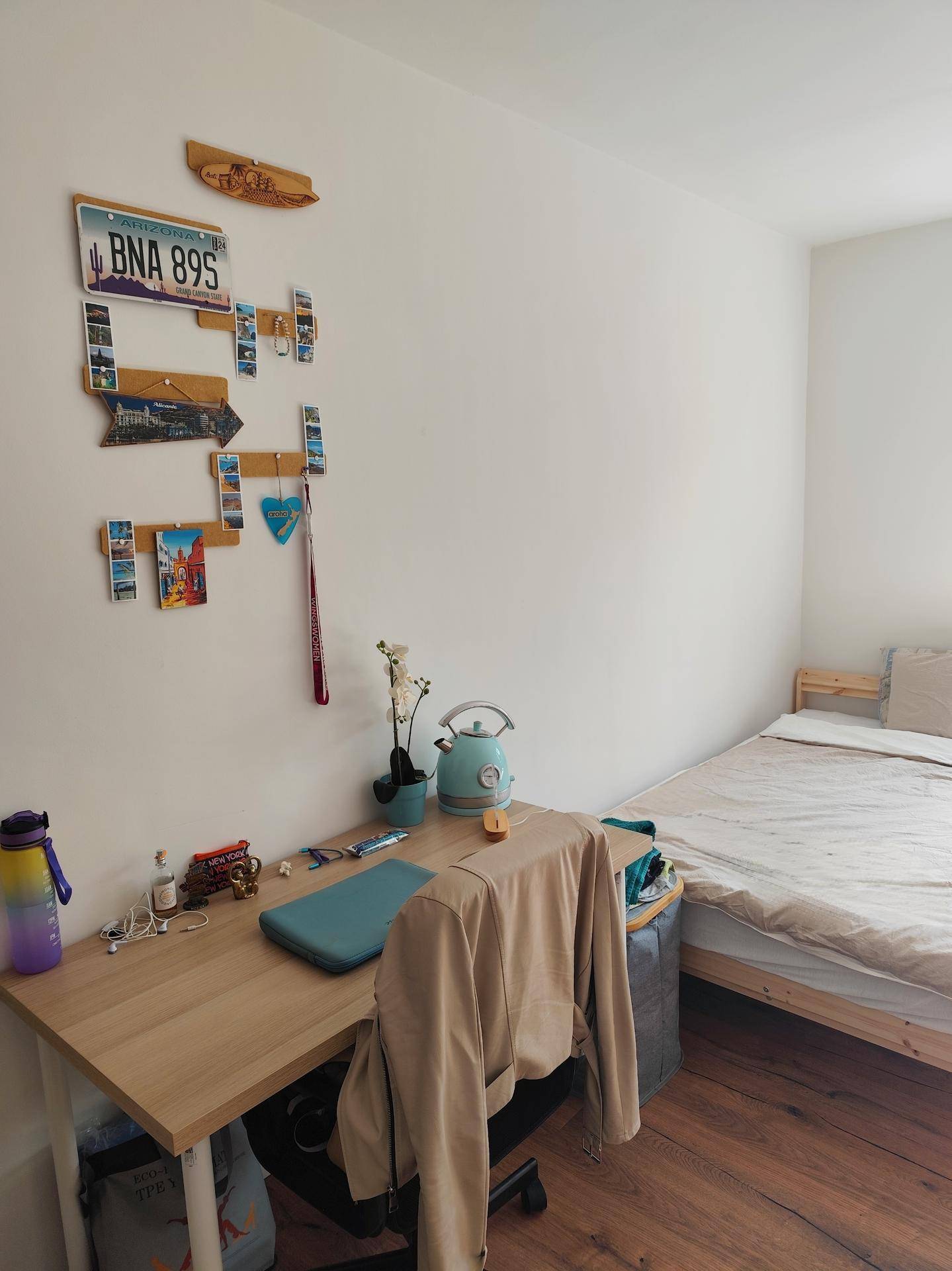 Gemütliches Schlafzimmer mit Schreibtisch, Holzboden und persönlichen Dekorationen an der Wand.