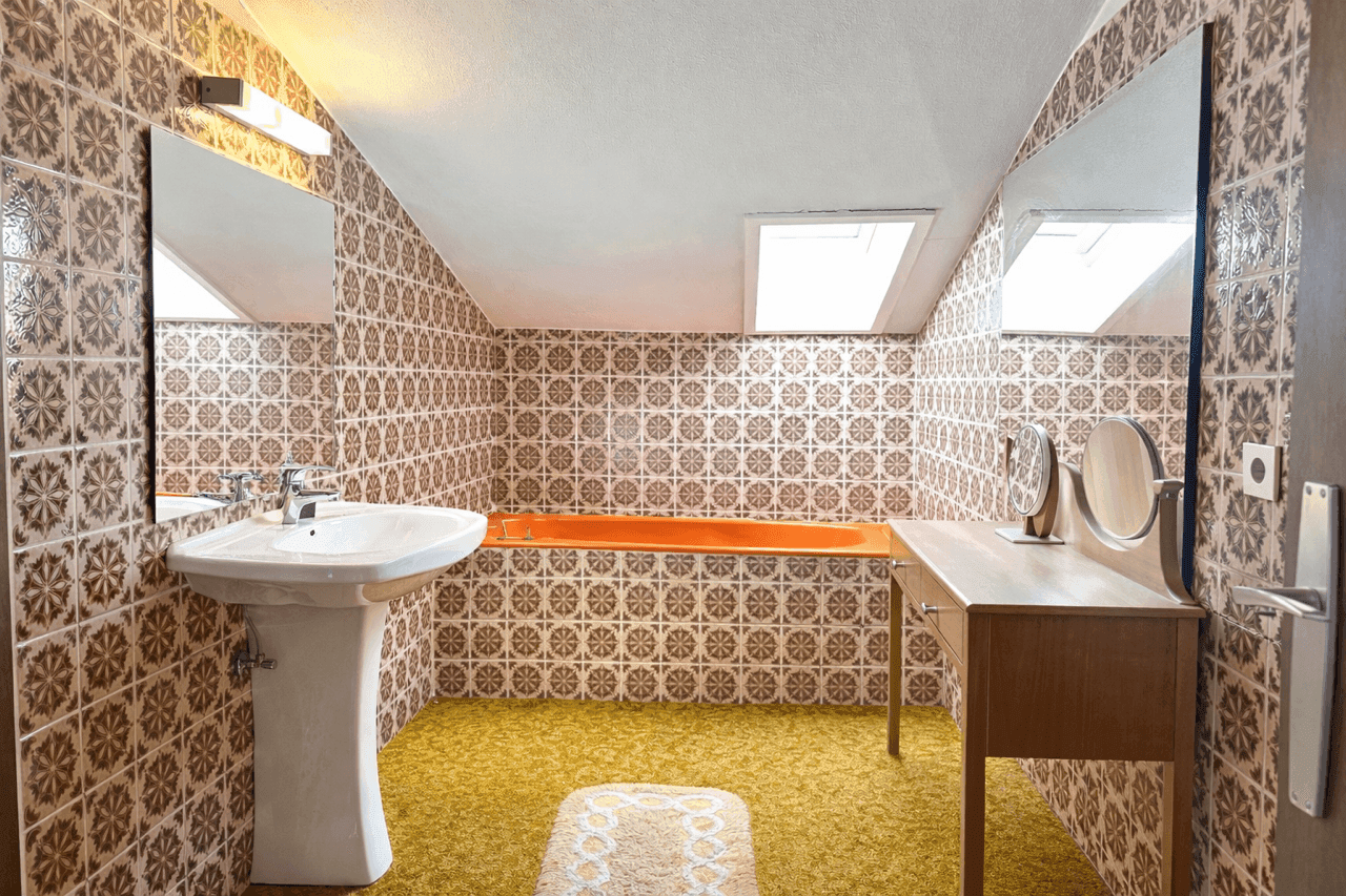 Badezimmer im Stil der 80er Jahre mit gemusterten Fliesen, orangefarbener Badewanne und Dachfenstern.