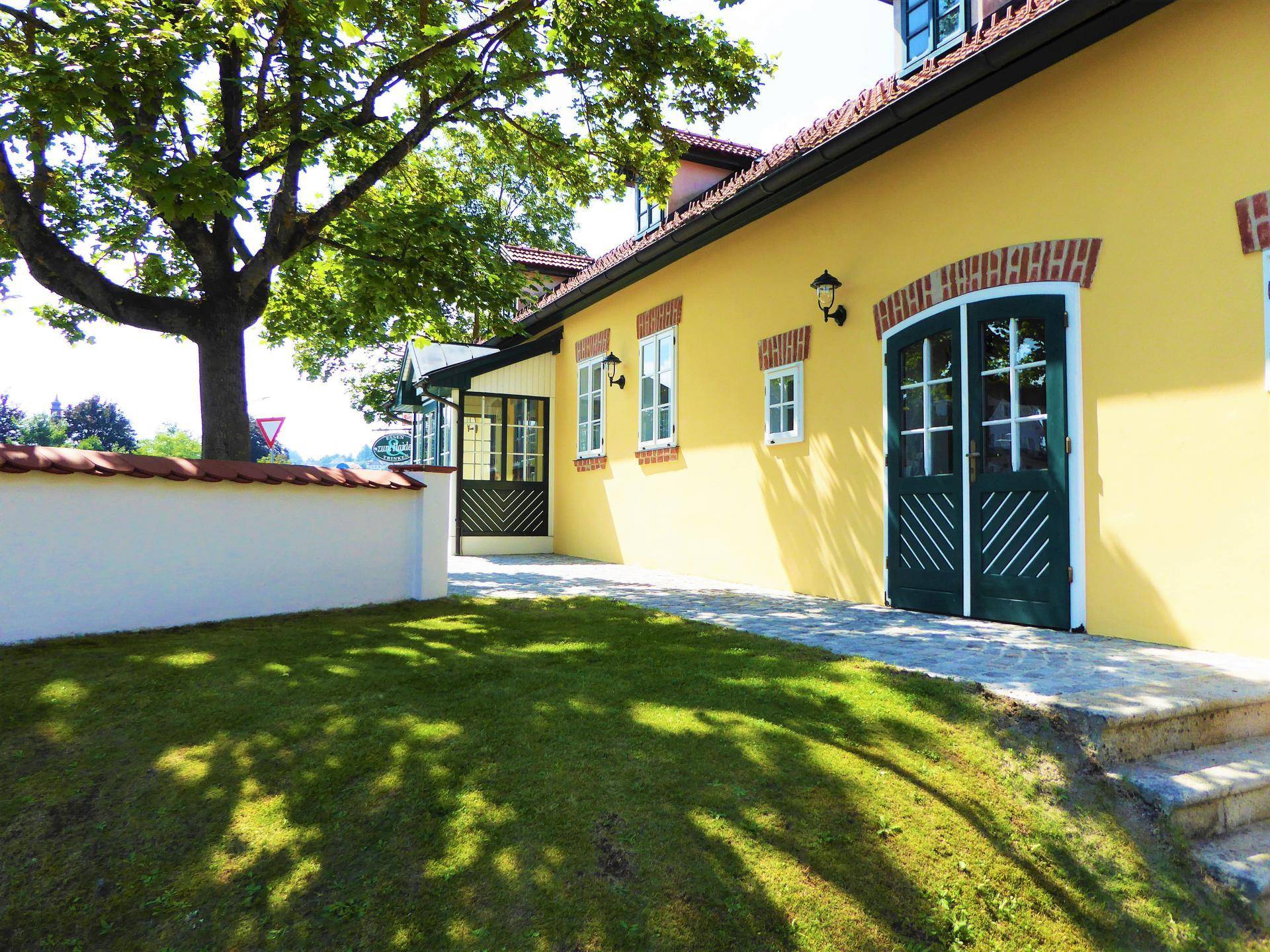 Traditionelles Gebäude mit gelber Fassade, grünen Türen und einem gepflegten Rasenbereich im Vordergrund.