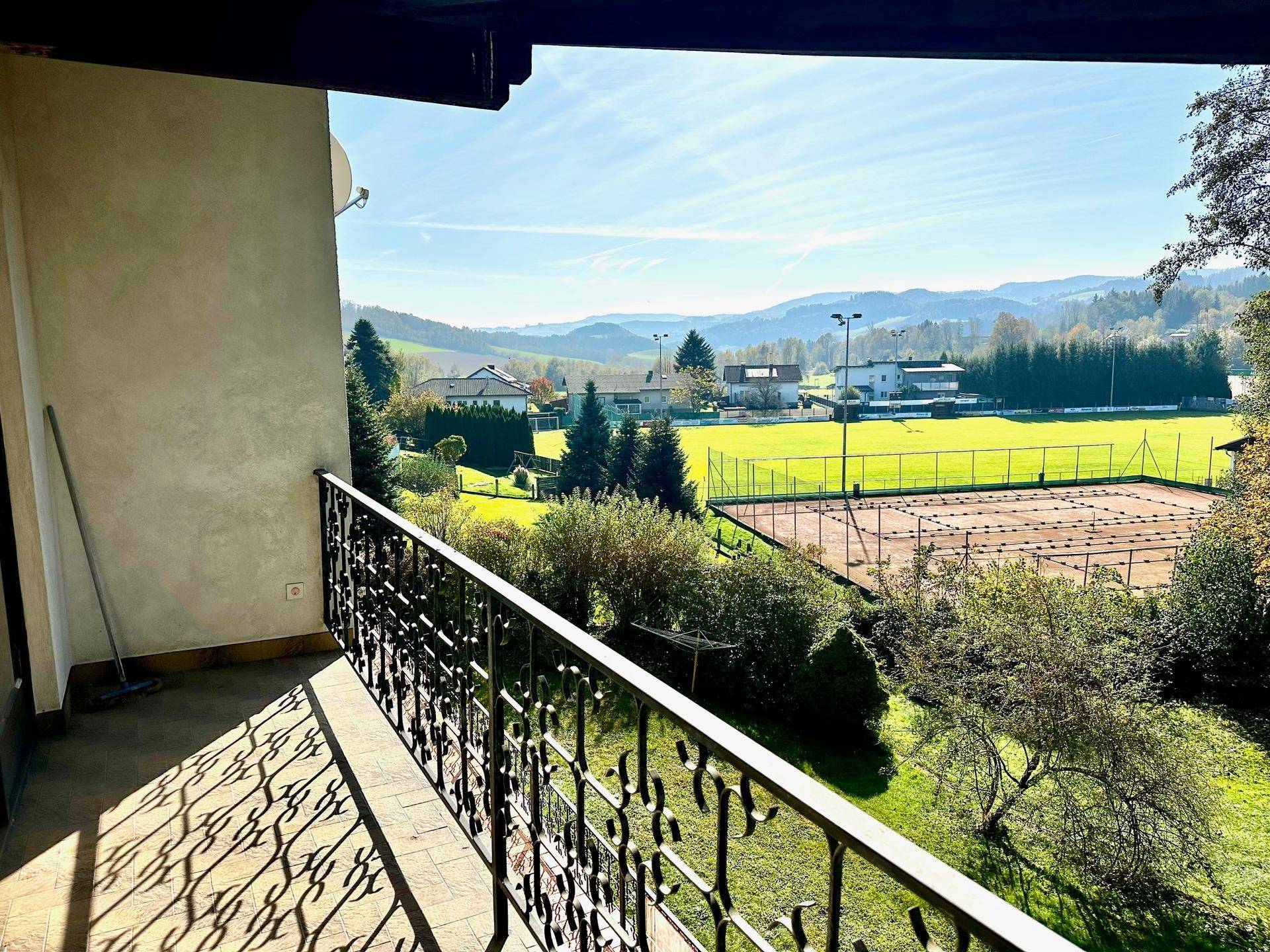 Balkon mit schmiedeeisernem Geländer und weitem Blick auf die grüne Landschaft und einen Tennisplatz.