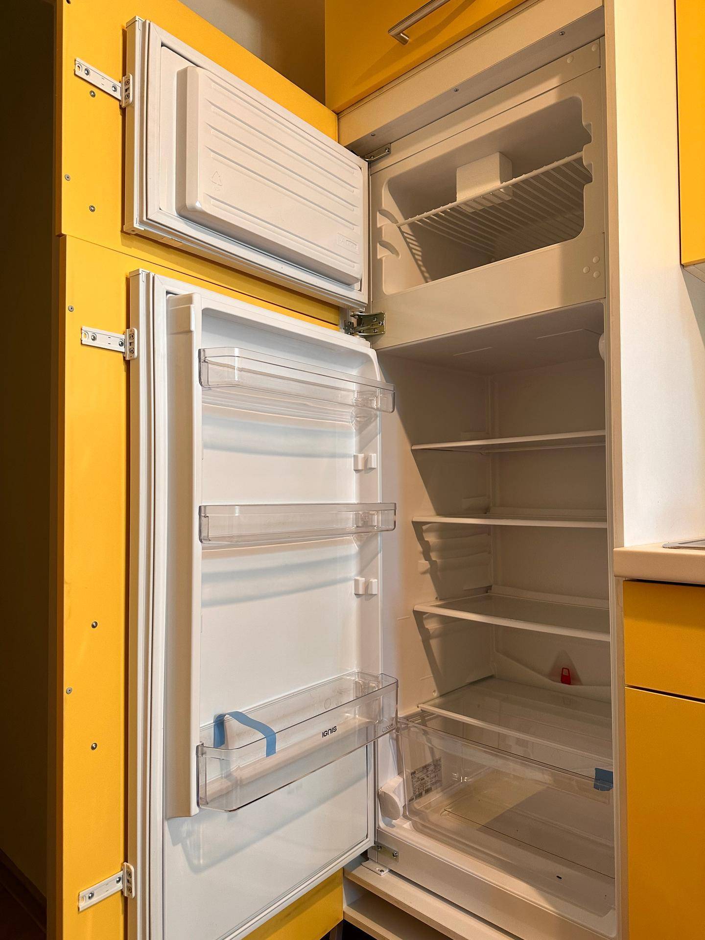 Offener Kühlschrank mit Gefrierfach, integriert in die gelbe Küchenzeile.