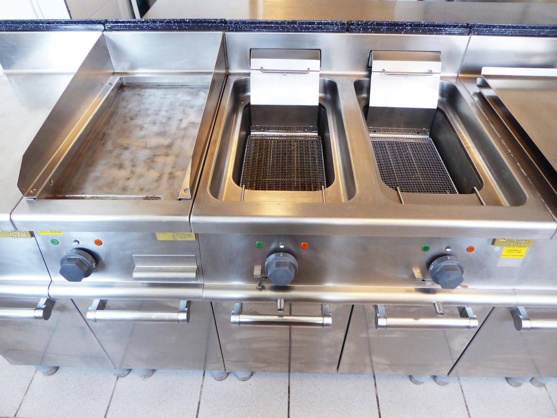 Nahaufnahme von professionellen Fritteusen und einer Grillplatte aus Edelstahl in einer Großküche.