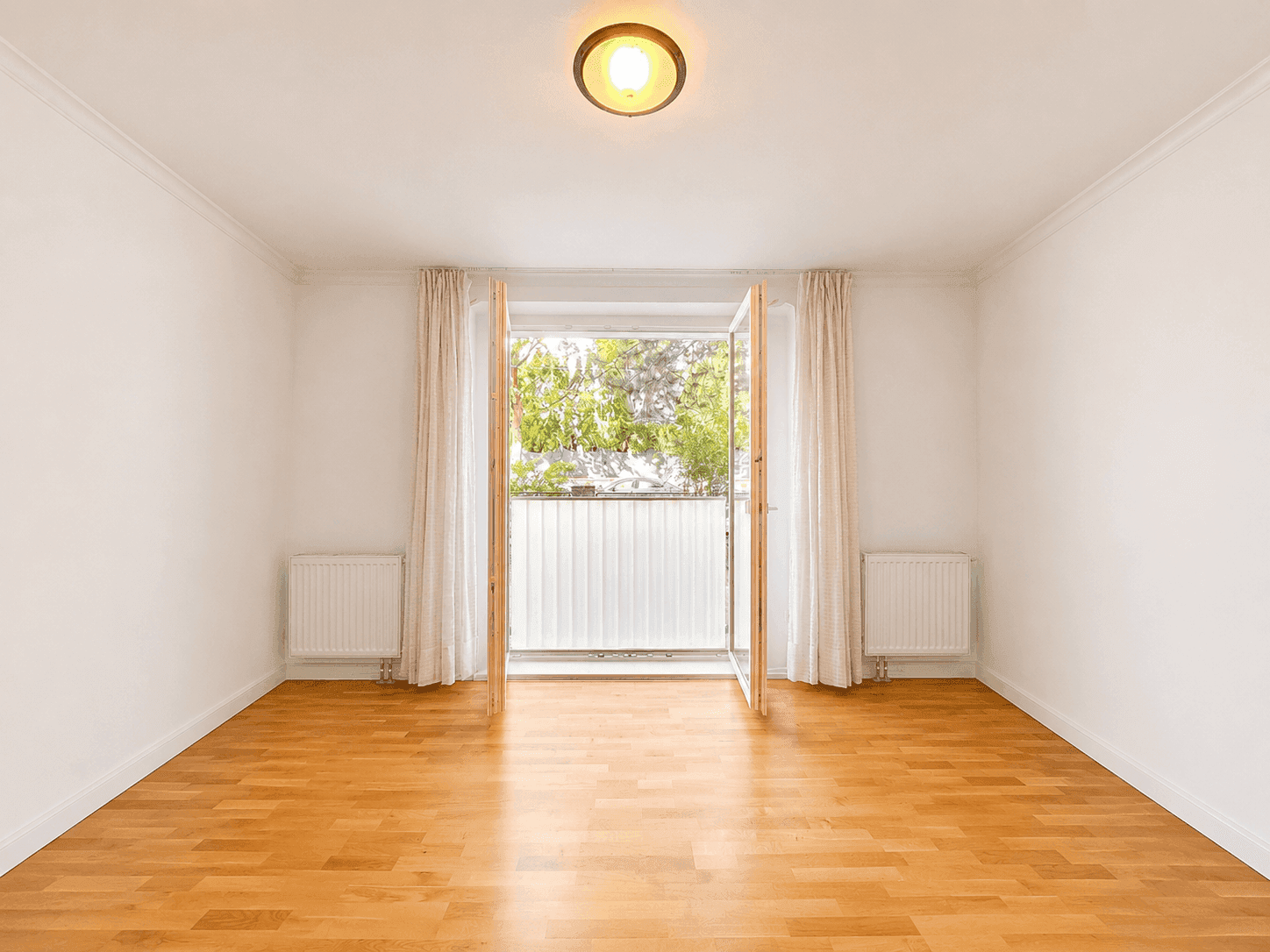Leerer Raum mit Parkettboden, weißen Wänden und Zugang zu einem kleinen Balkon.