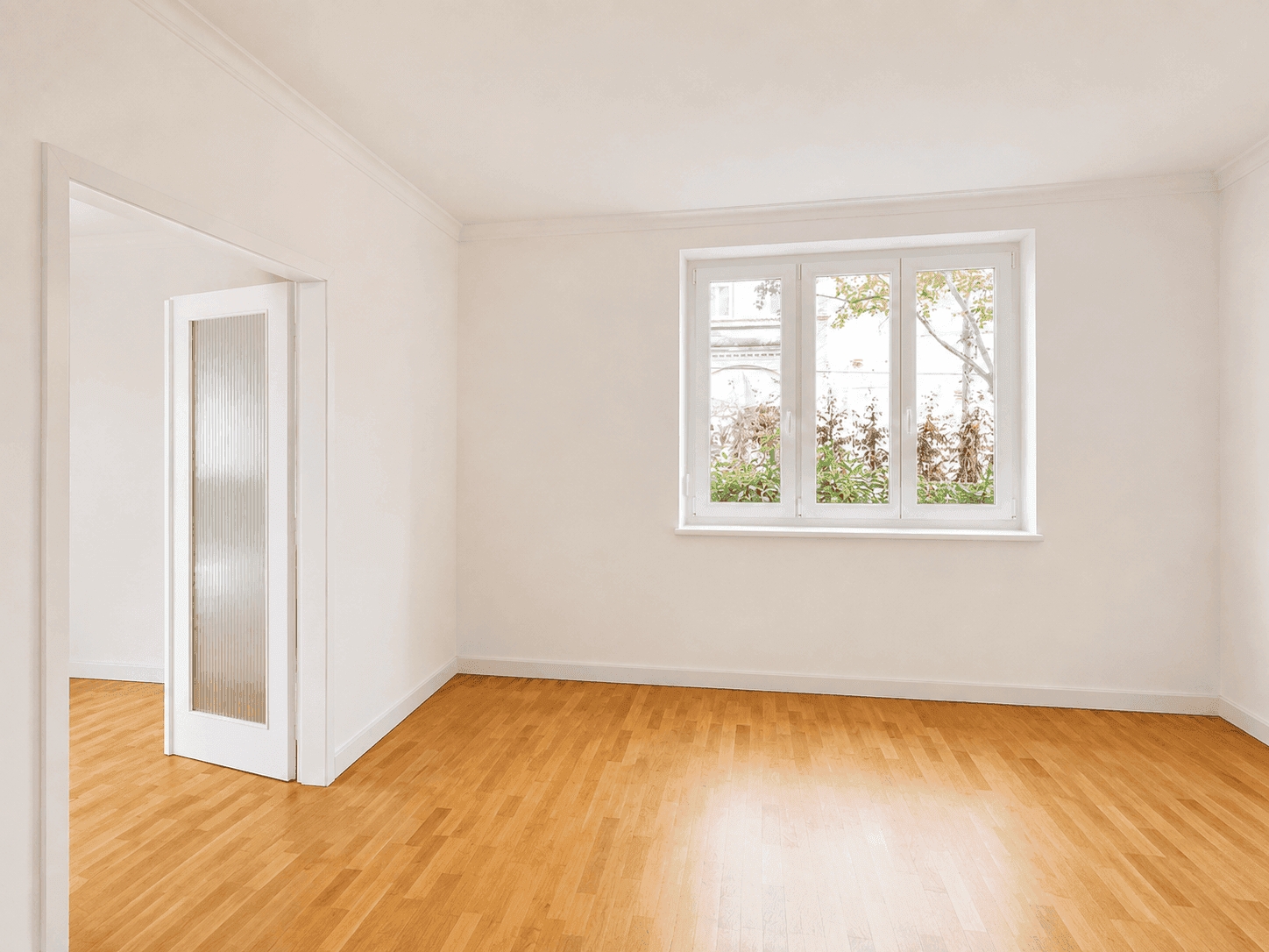 Heller Raum mit Parkettboden, weißen Wänden und einer Tür zu einem weiteren Zimmer.