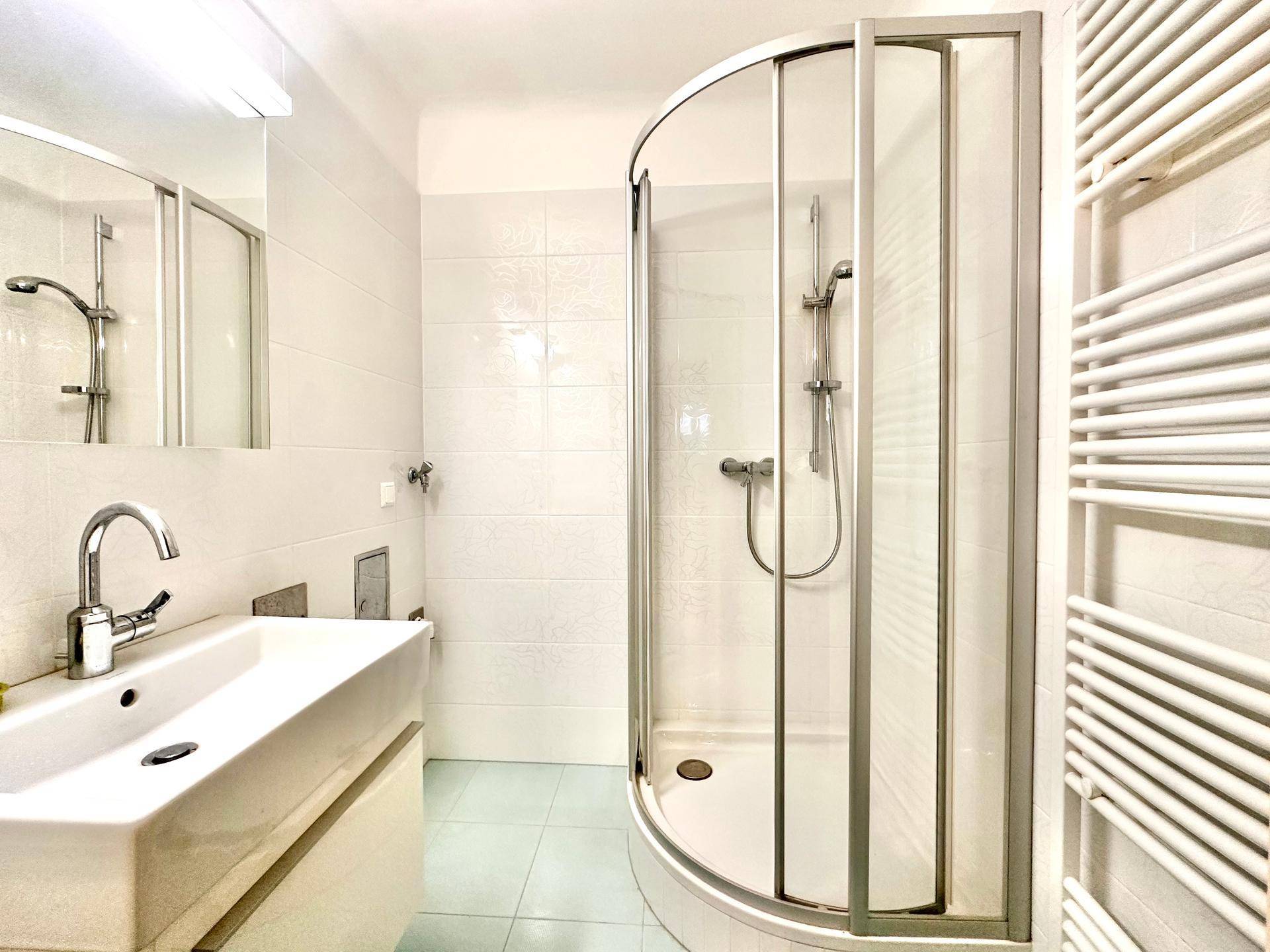 Badezimmer mit Duschkabine, Waschbecken und einem praktischen Handtuchheizkörper.